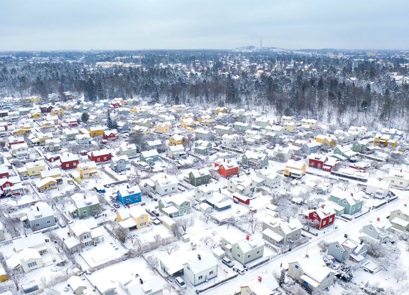 Flygbild över snötäckt villaområde med färgglada hus en vinterdag.
