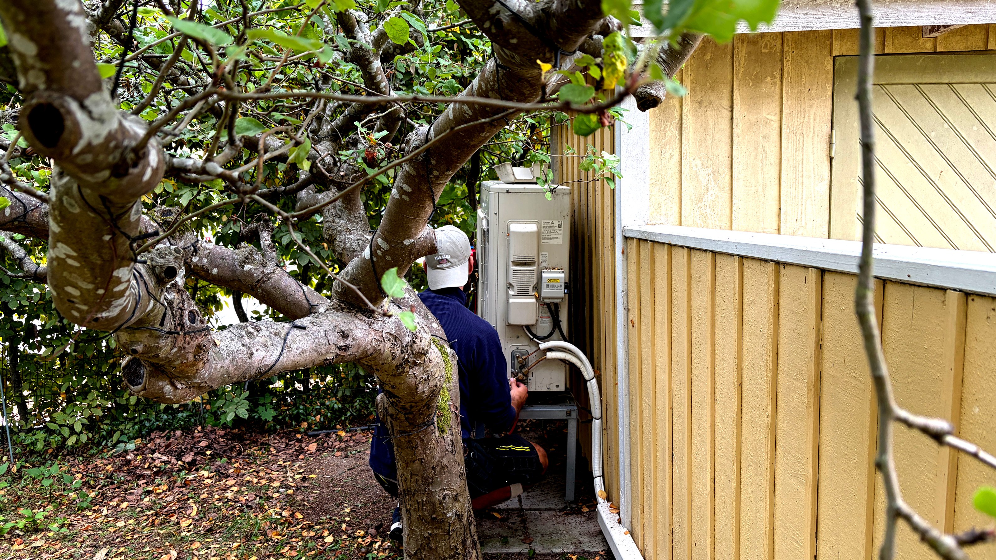 Värmepumpstekniker arbetar med utedelen till en luft-vattenvärmepump utanför ett hus.