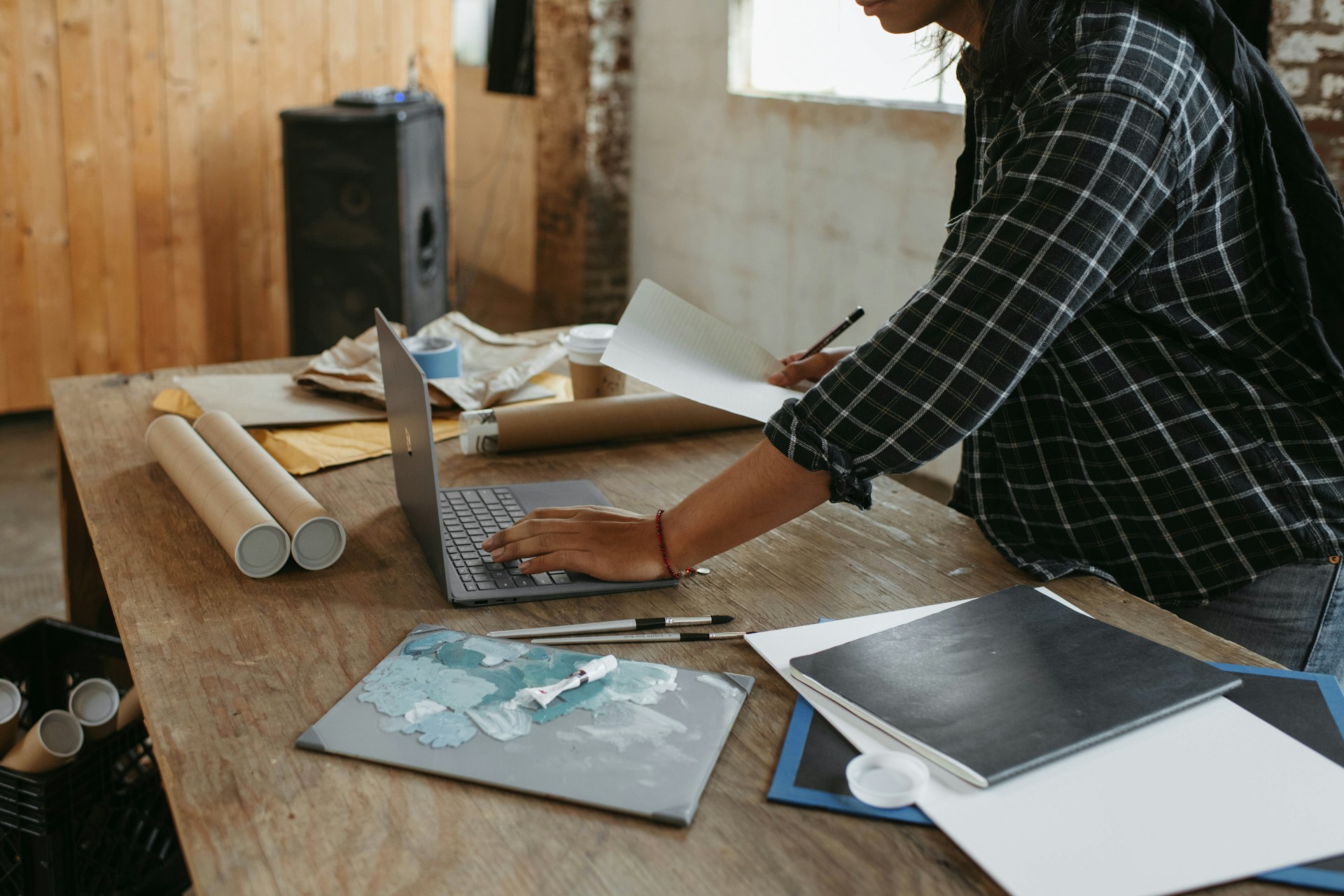Woman by a woodworking desk working on laptop and drawing