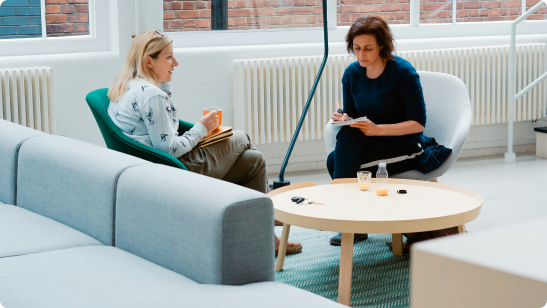 Two colleagues in conversation on lounge chairs in a modern office