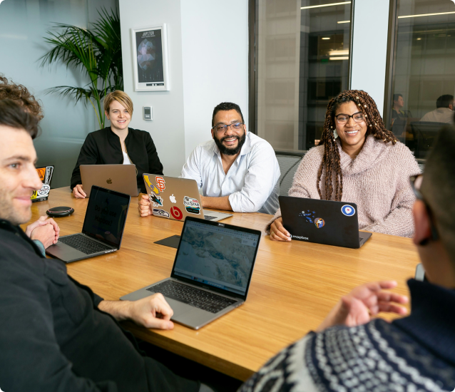 A team collaborating around a table covered with laptops and notes