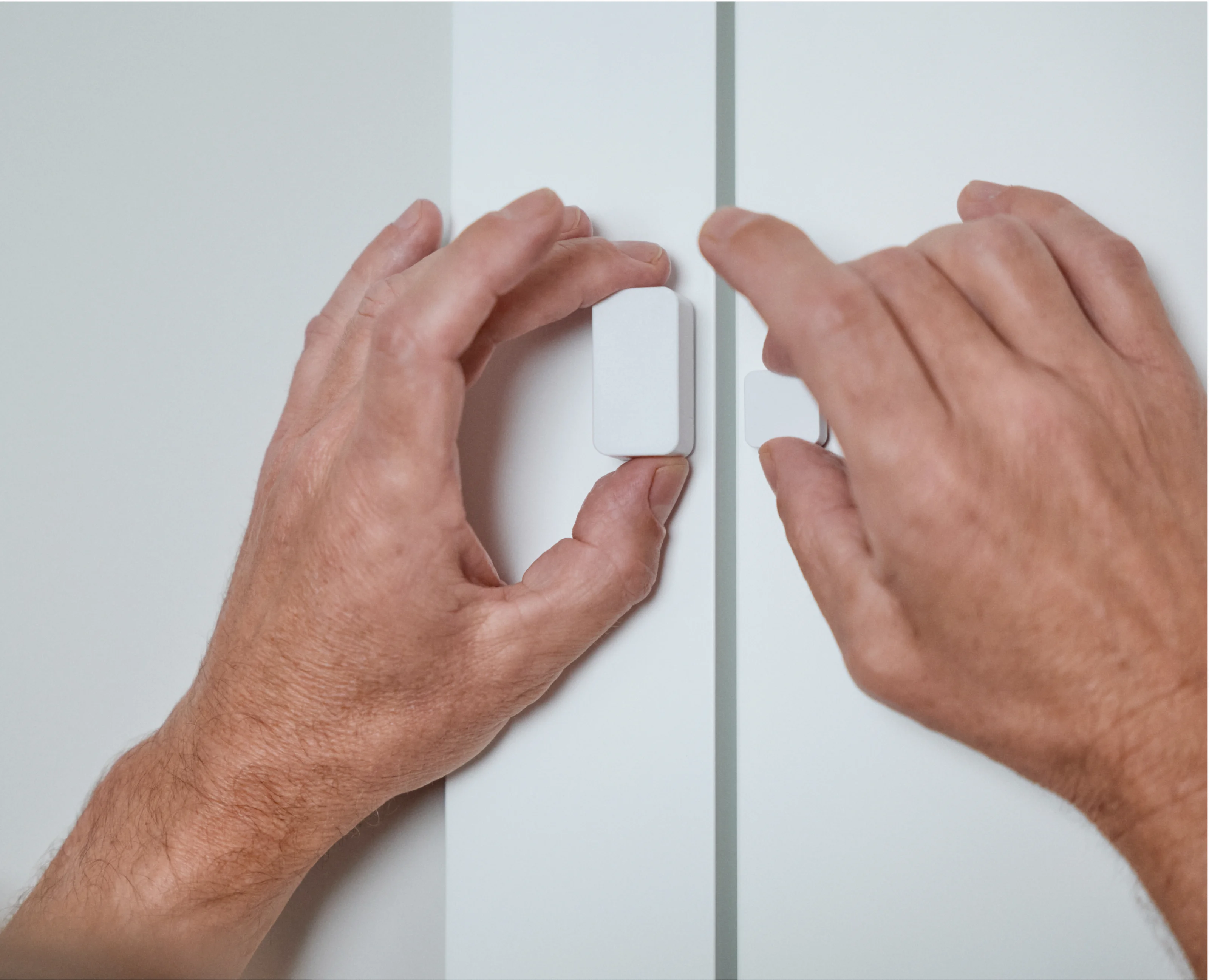 Hands installing the Nuki Door Sensor on a door frame.