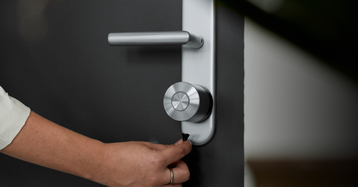 The Smart Lock Ultra installed on a black door with silver hardware. A hand attaches the charging cable to the Lock.