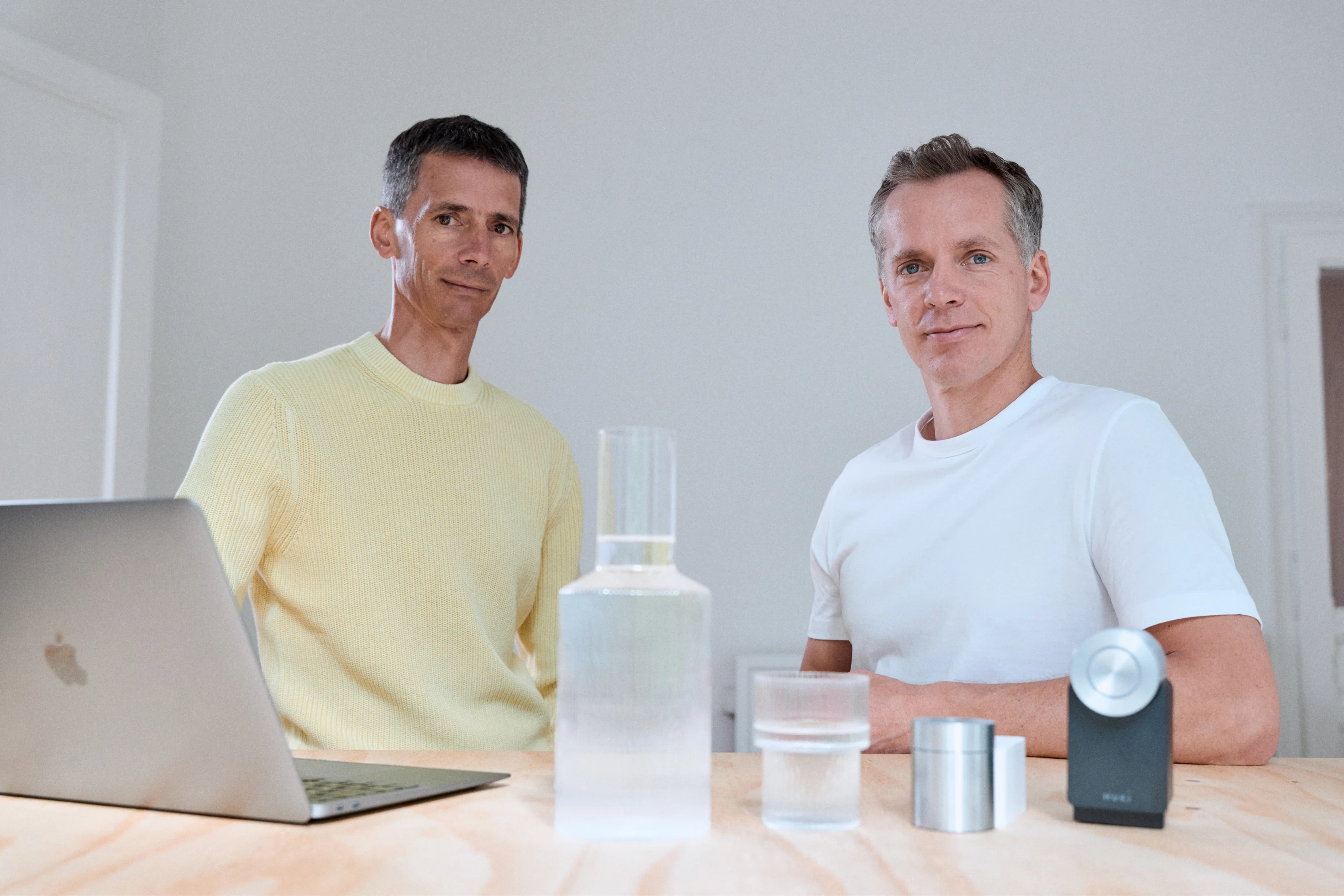 Martin and Jürgen Pansy, founders of Nuki, sit at a table with a laptop and a Nuki Smart Lock in a bright room.