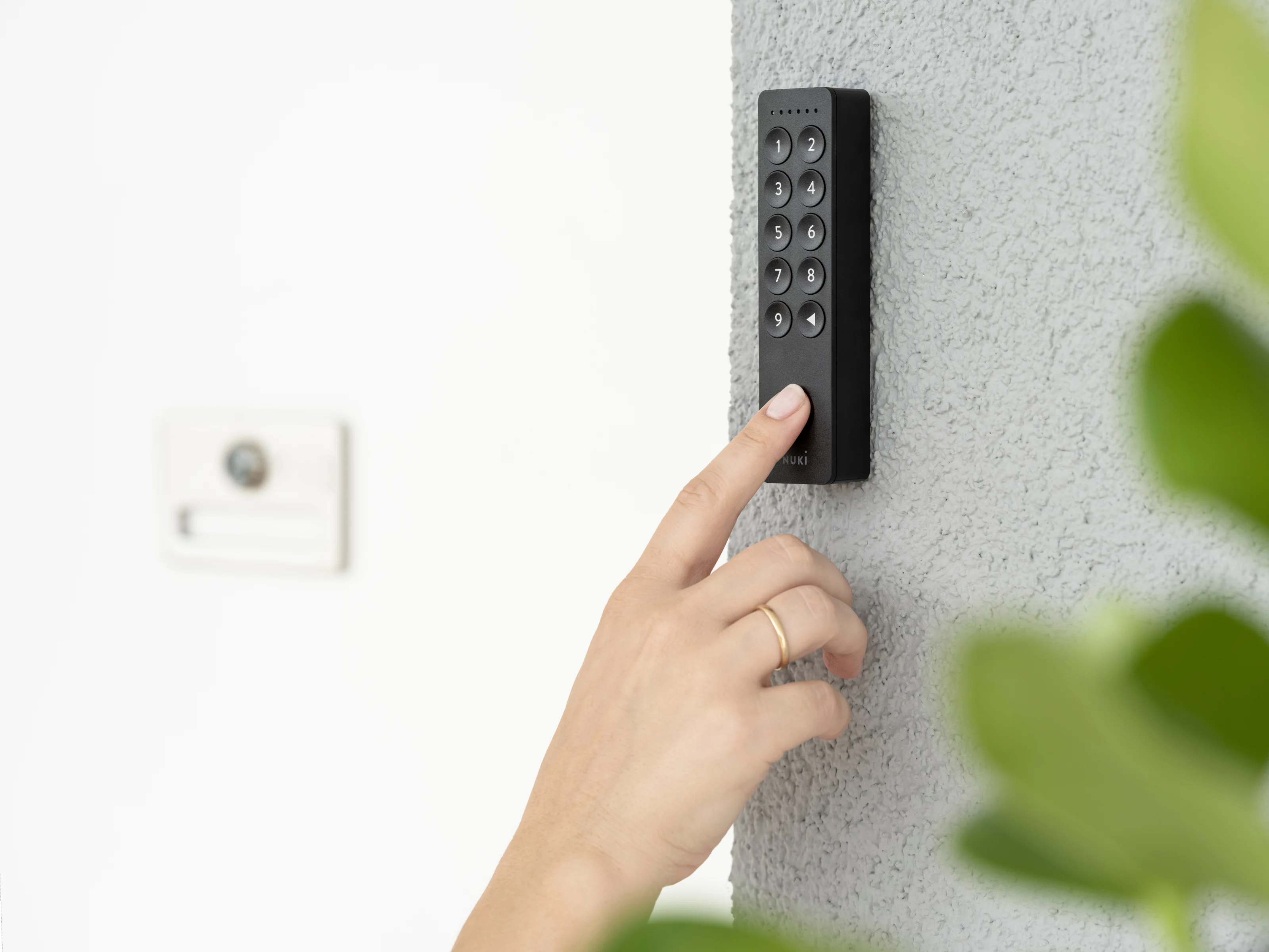 Hand of a person with a ring using a keypad on a gray wall outdoors.