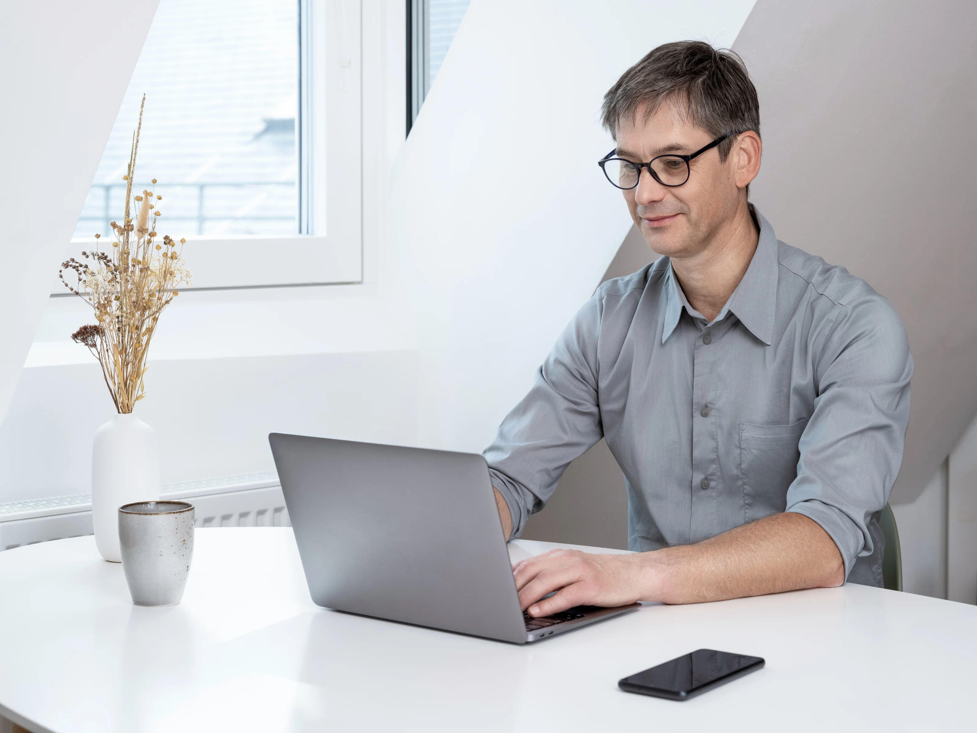 Person sitting at a desk working on a laptop, with a smartphone and a coffee mug on the table.