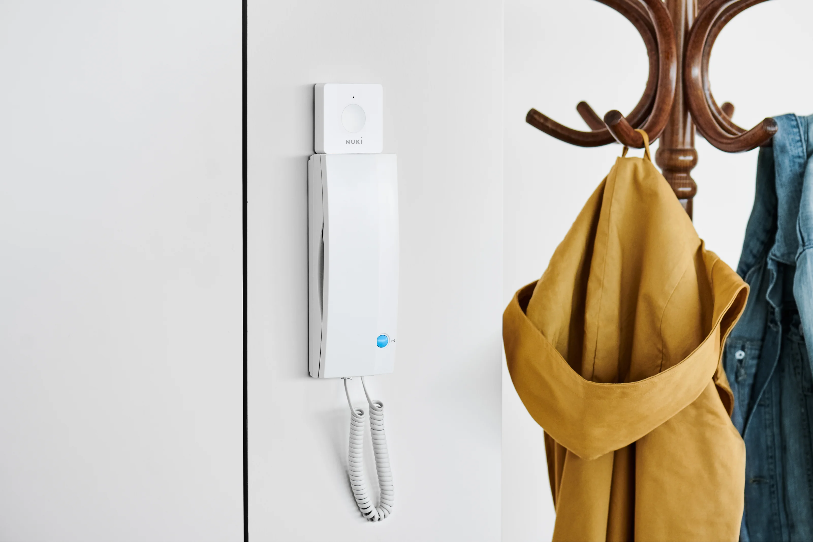 Nuki Opener installed on an intercom next to a coat rack with jackets.