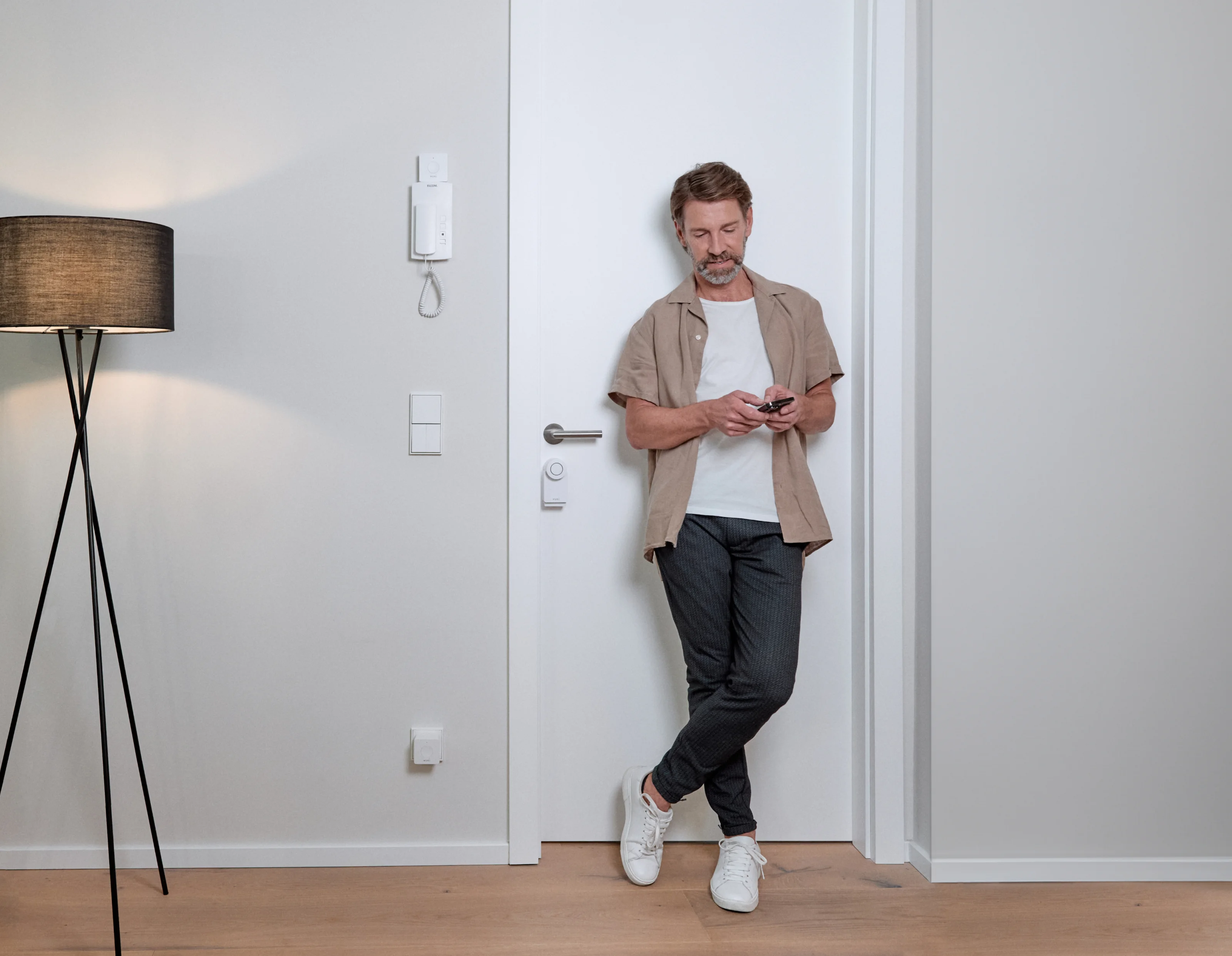 Man in front of the entrance door with the Smart Lock on it installing the Nuki app on his smartphone.