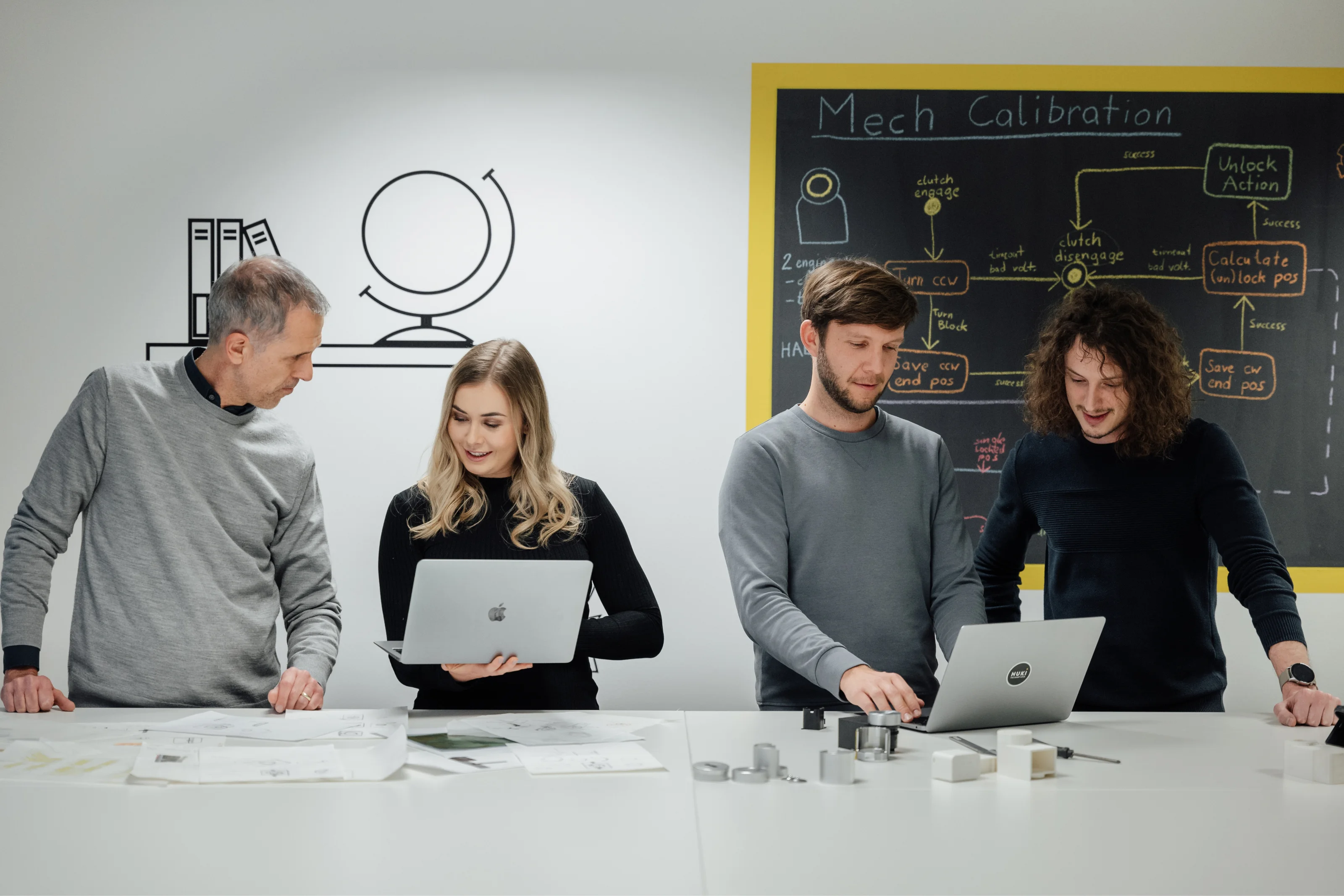 Nuki team members collaborate in front of a chalkboard during a development session with laptops and sketches.