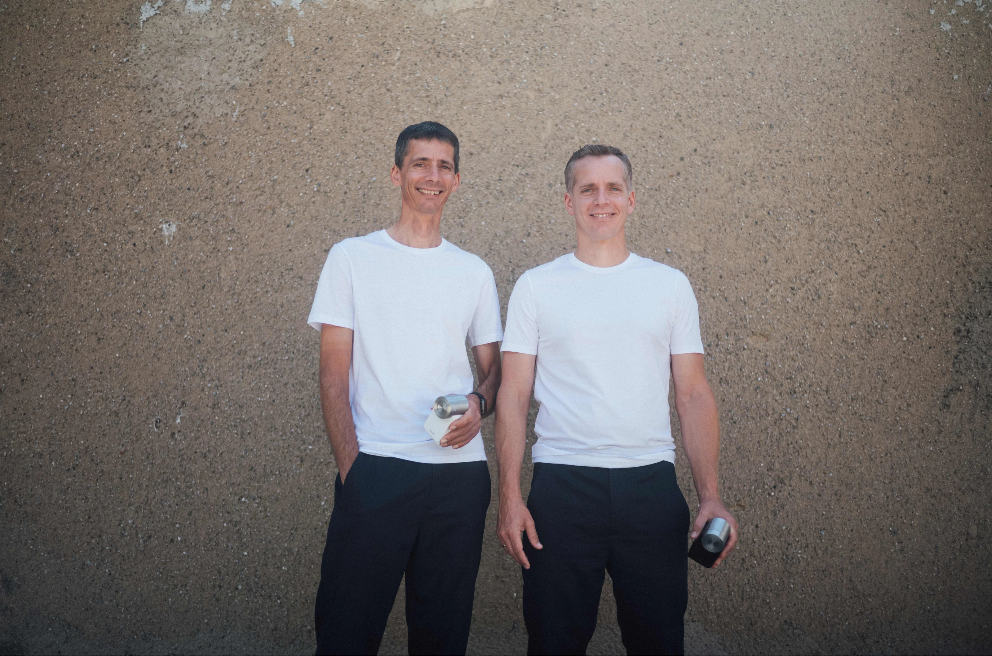 Nuki founders Martin and Jürgen Pansy stand smiling in white shirts, each holding a Nuki Smart Lock.