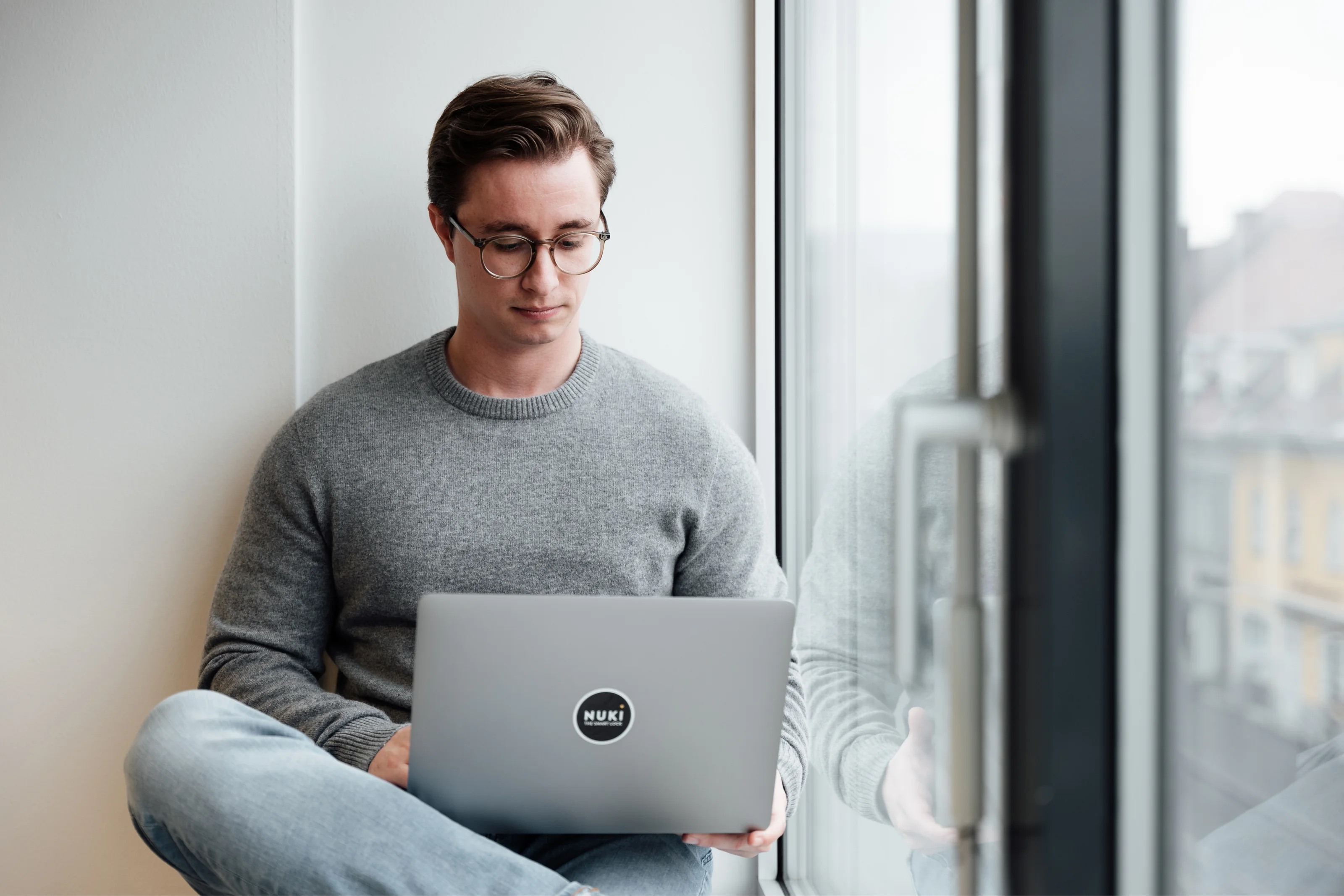 Nuki team member works on a laptop with Nuki sticker while sitting by the window in a bright office.