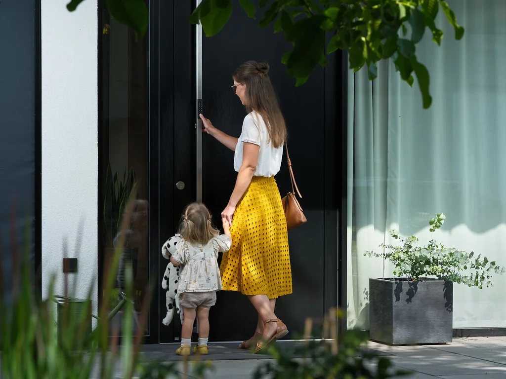 Mother and child standing at a modern front door, with the mother unlocking it using a smart keypad