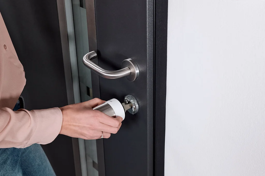 Woman installing a white Nuki Smart Lock Pro on a dark door with silver hardware.