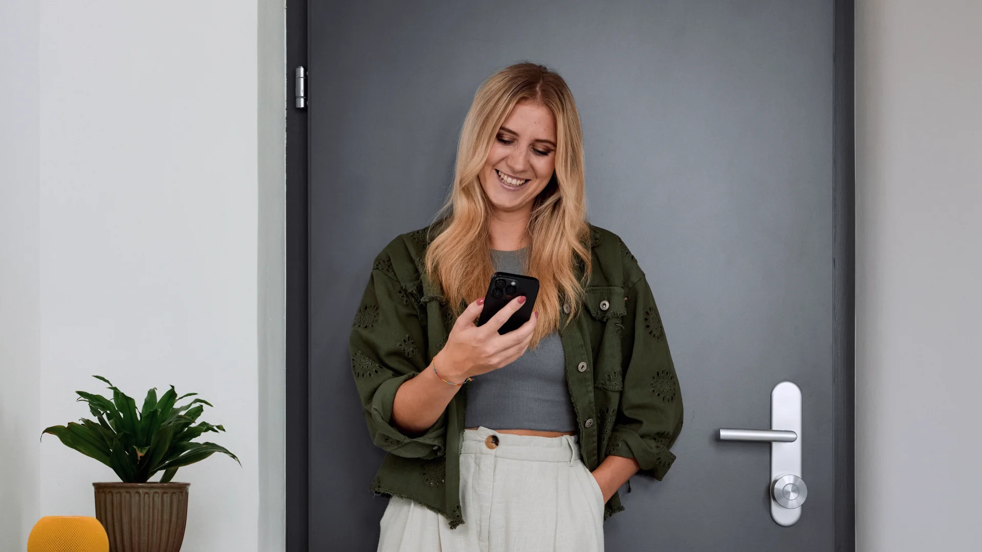Woman standing in front of her door, smiling while using the Nuki app – smart access with a tap.