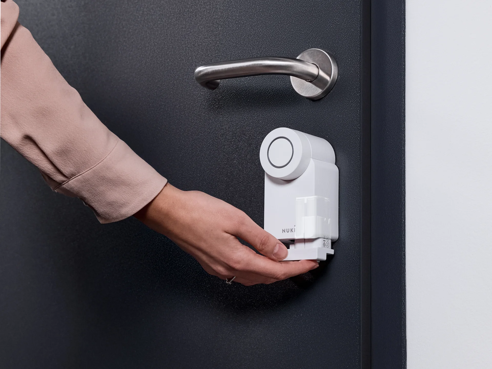 Woman inserting the Nuki Power Pack into a white Smart Lock Pro on a dark door with silver handle.