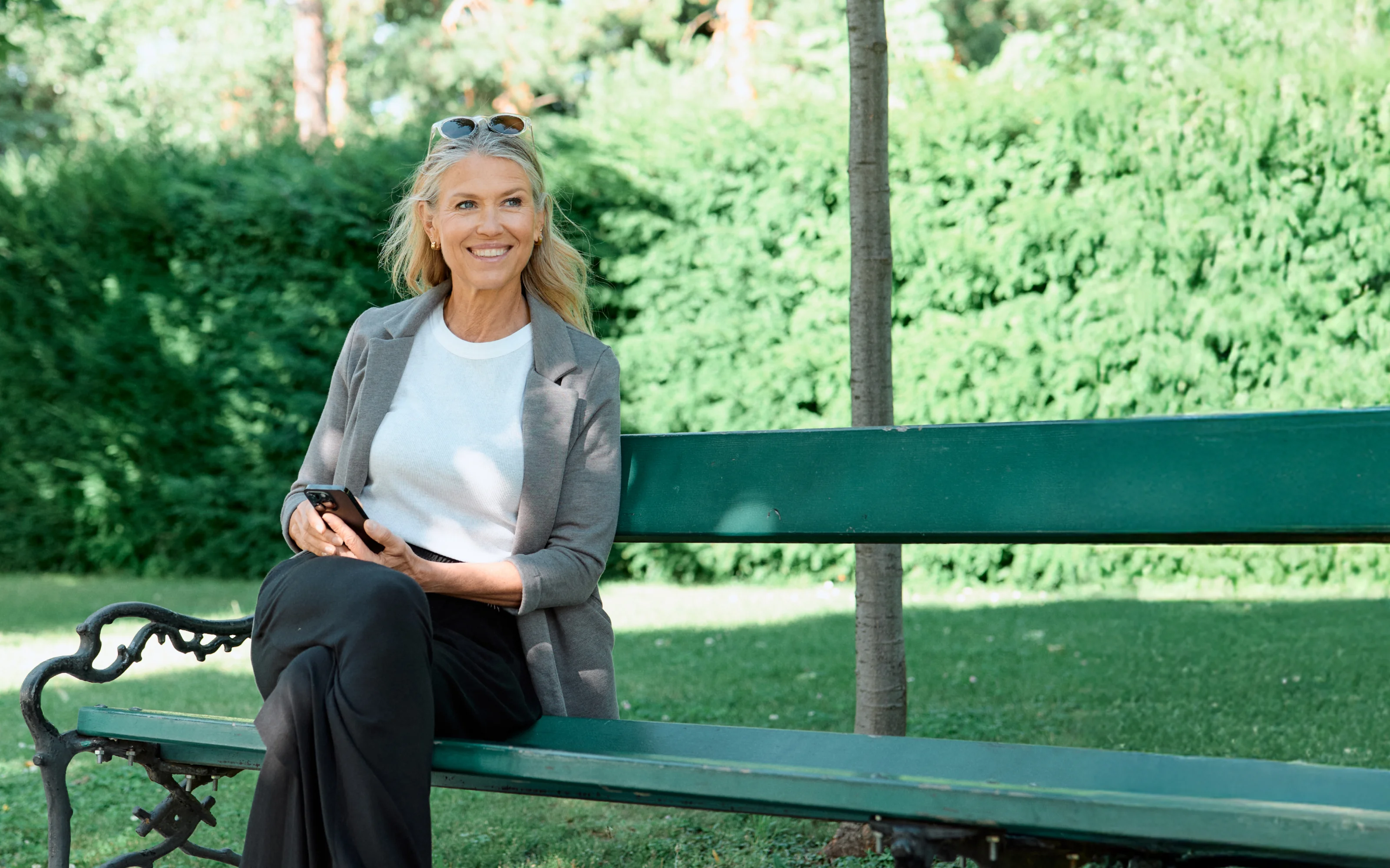 Smiling woman sitting on a park bench holding her smartphone.