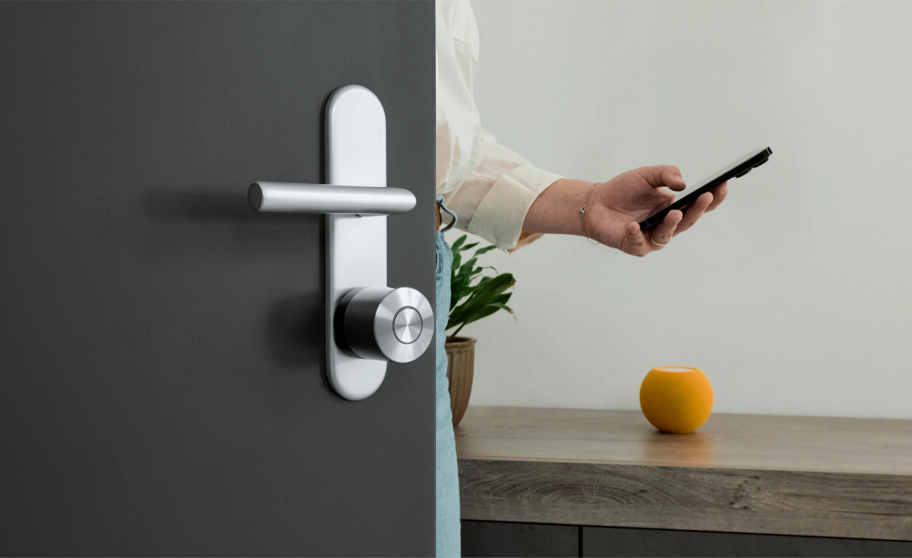 Woman entering a room via a black door with a Nuki Smart Lock Ultra. An Apple HomePod mini is on the sideboard.