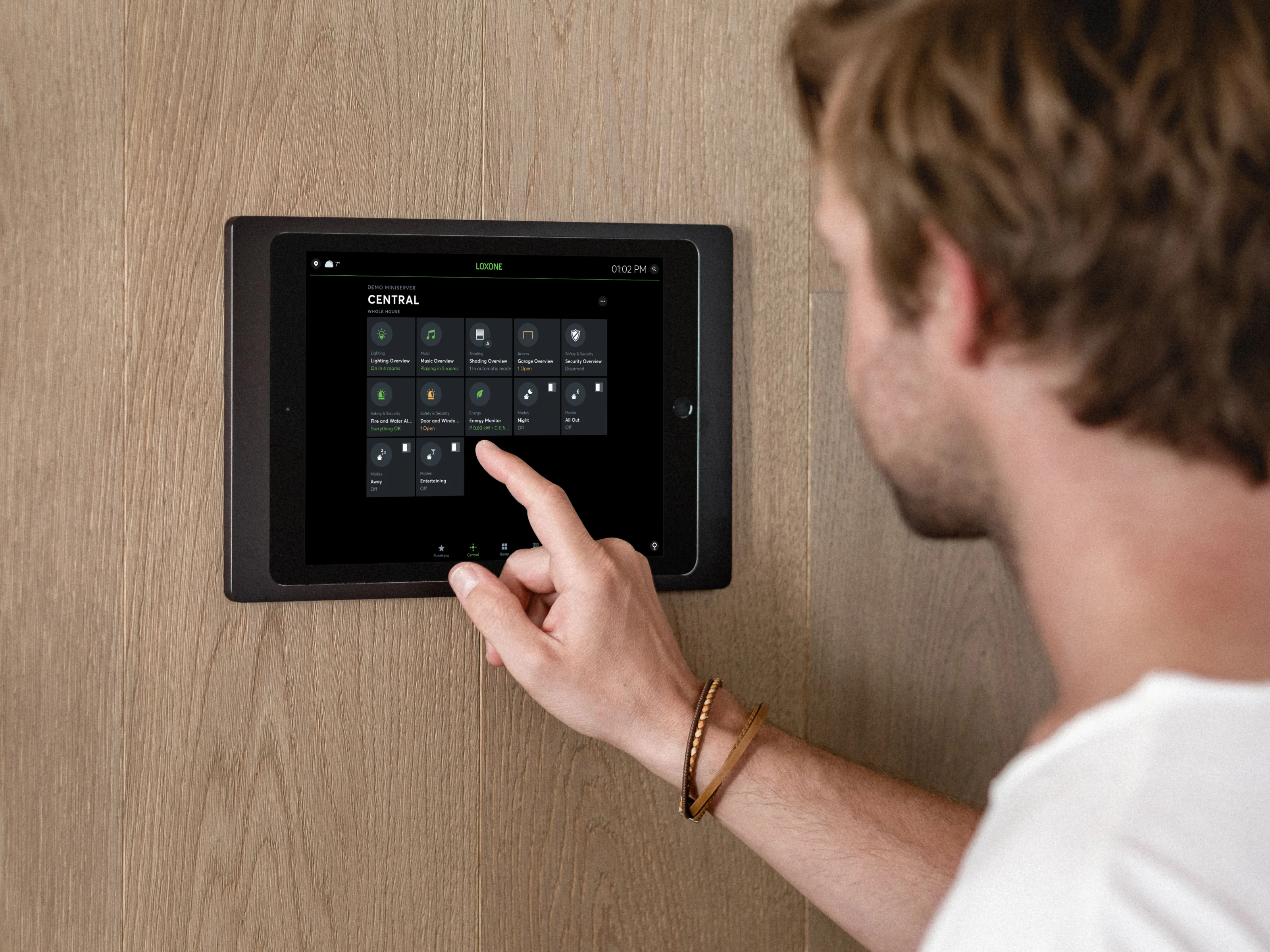 Man controls smart home functions on a wall-mounted tablet using the Loxone app.