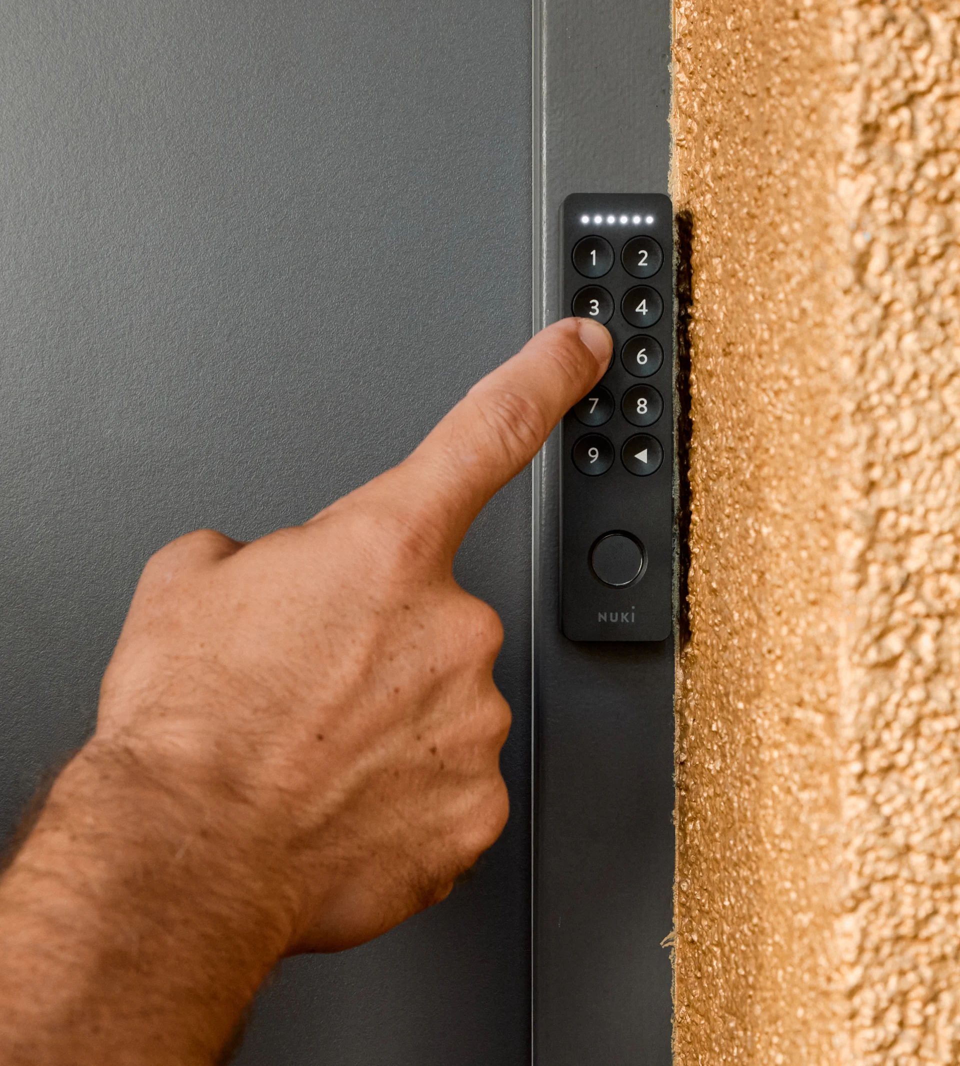 Close-up of a hand pressing the number 3 on a Nuki smart lock keypad mounted on a wall.