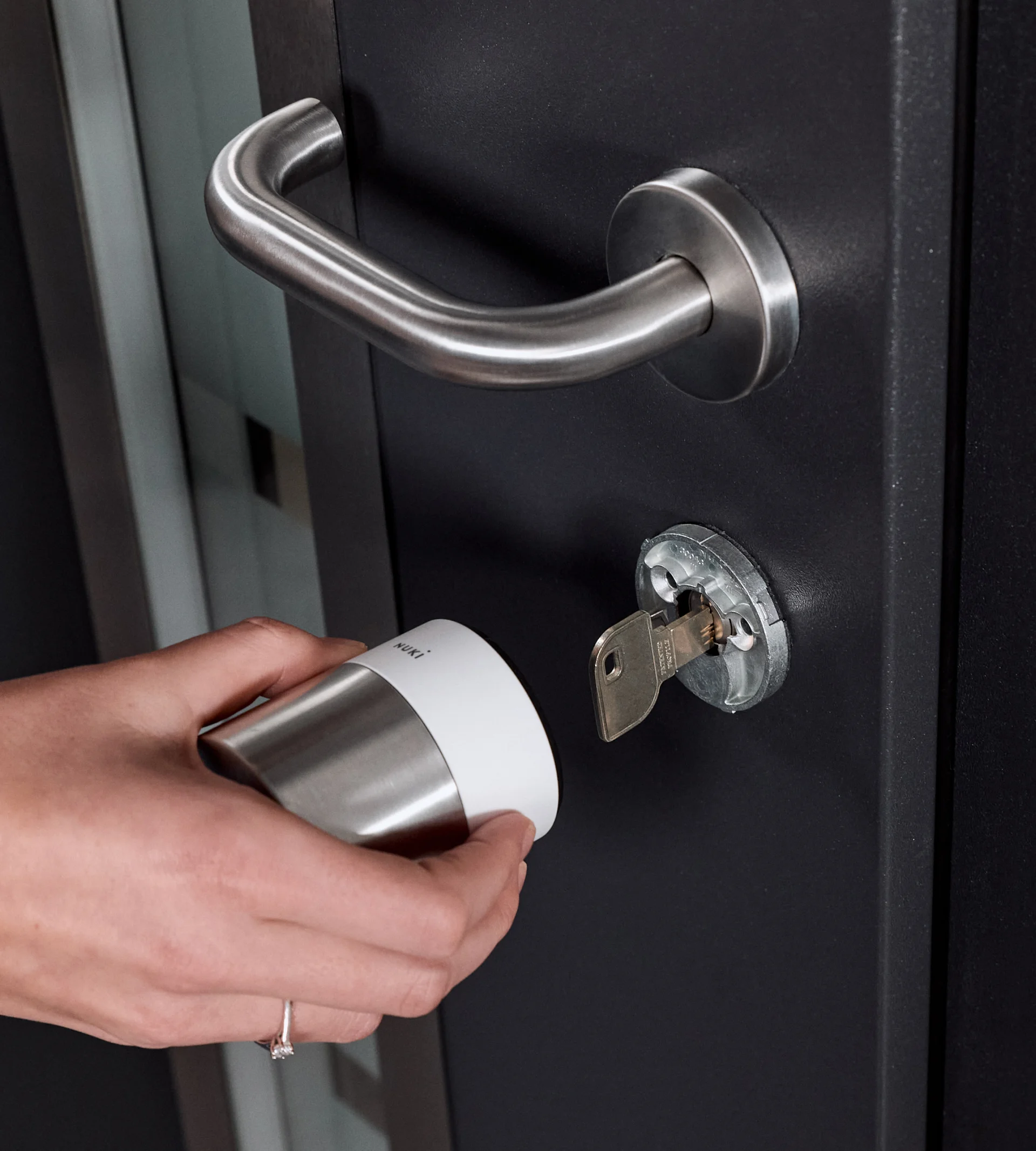 A female hand installing the Nuki Smart Lock Pro with the white ring on a black door with silver hardware