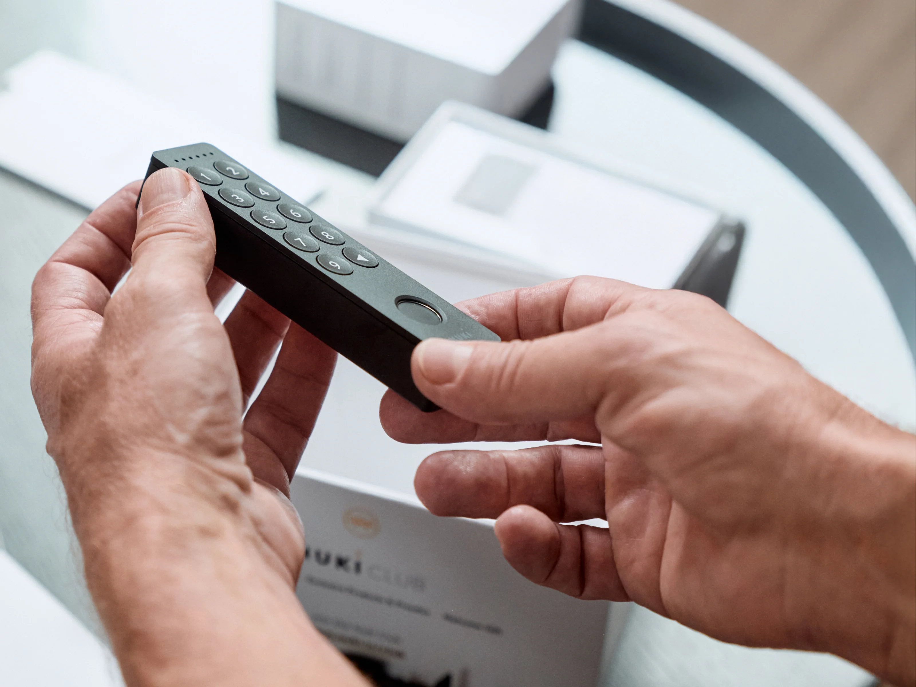Hands holding Nuki Keypad 2 with fingerprint sensor and numeric keys.