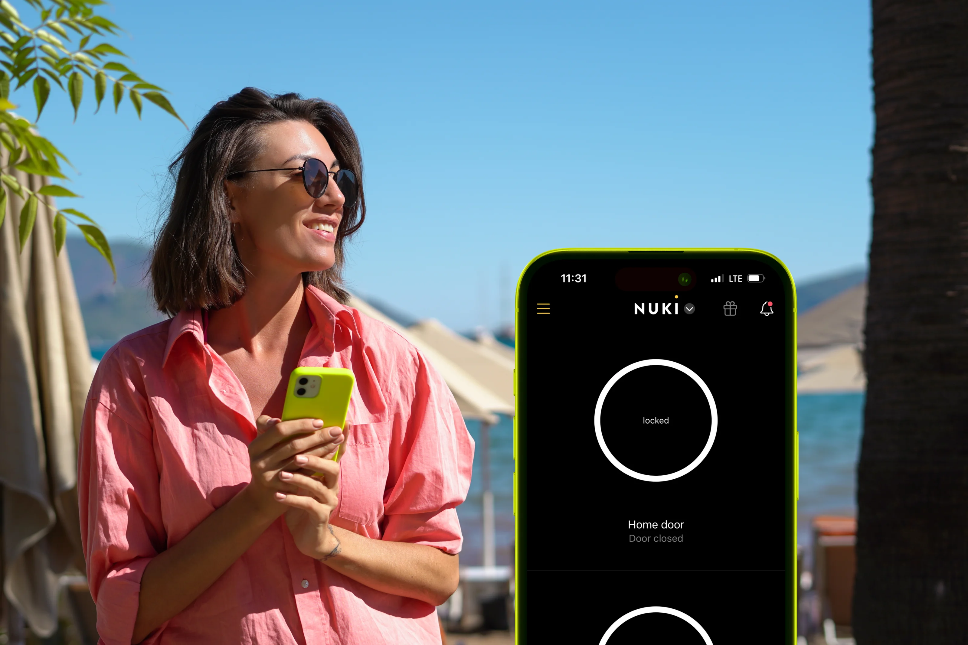 Woman in pink shirt with phone at a holiday spot. A phone screen shows the Nuki app.