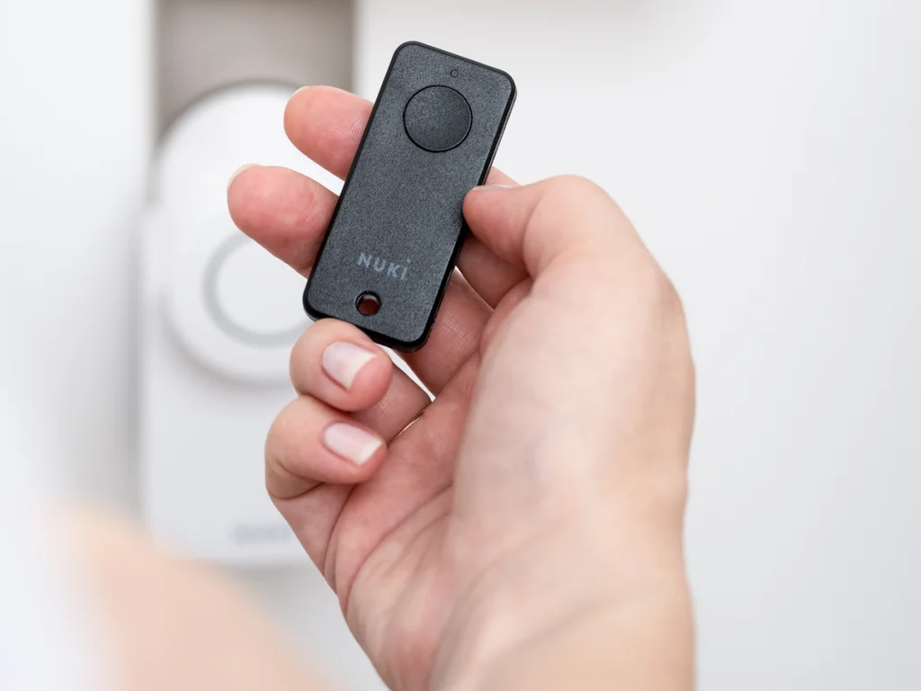 A hand holding the Nuki Fob in front of a Smart Lock Go