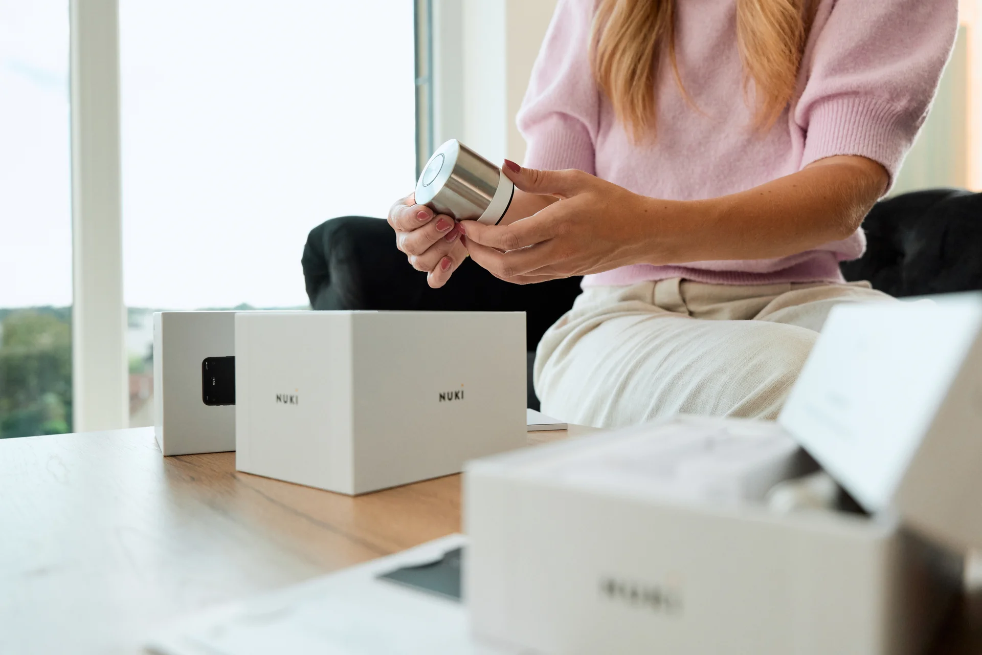 A table with Nuki Smart Lock boxes on top and a woman in the background taking out a Smart Lock Ultra.