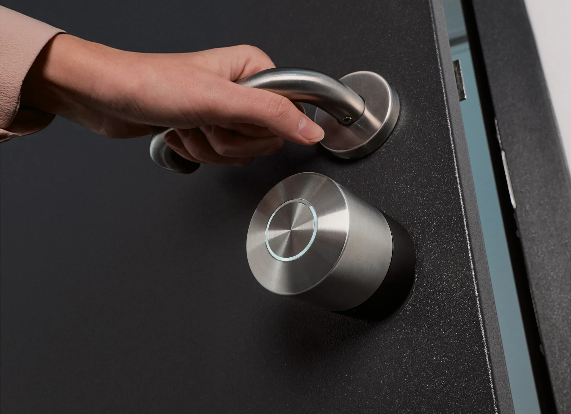 Hand opening a door equipped with the Nuki Pro smart lock mounted below a silver door handle.