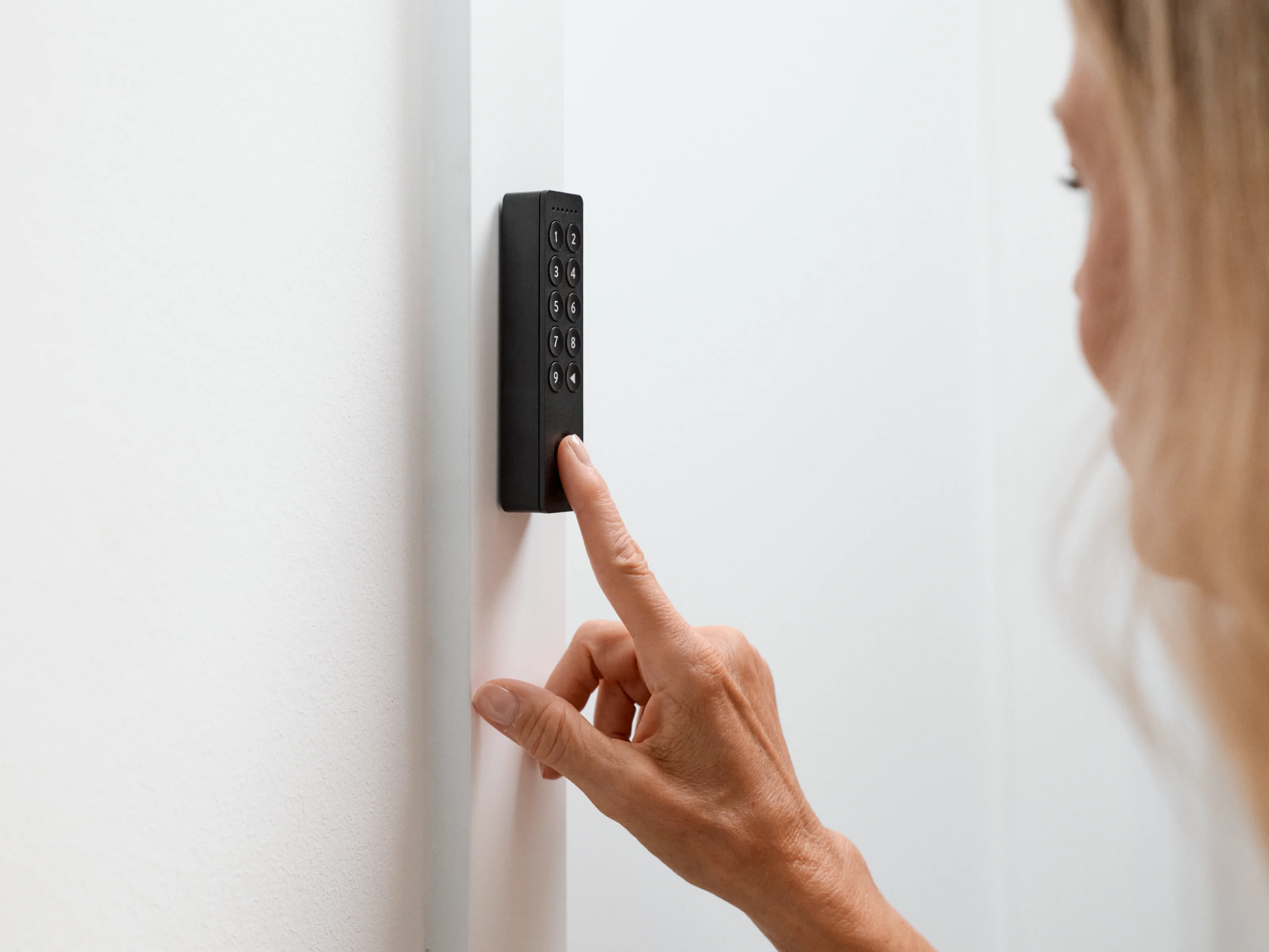 Woman presses the fingerprint sensor on the Nuki Keypad 2 mounted on a white wall.