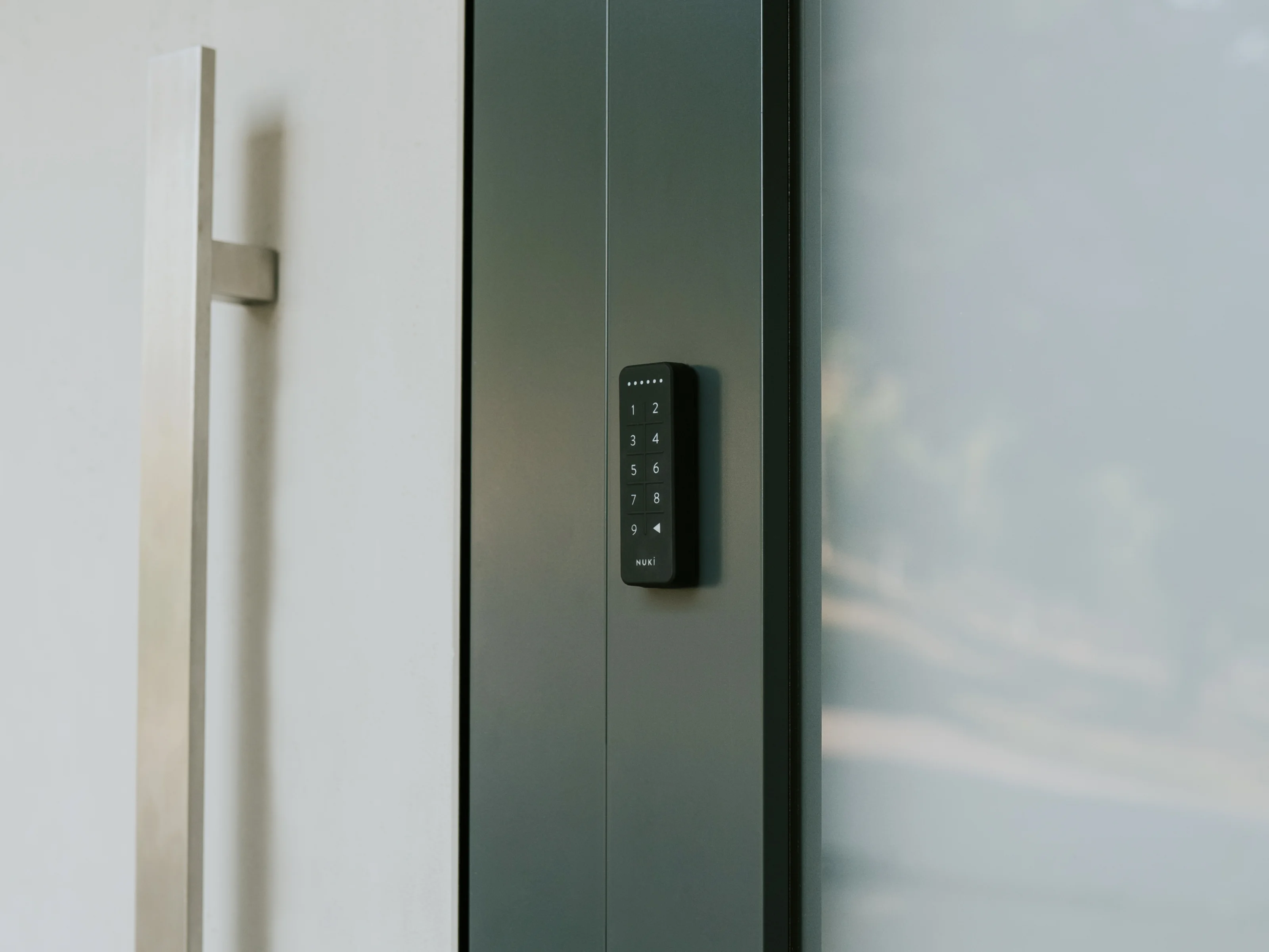 The Nuki Keypad mounted on a dark modern door next to a sleek silver door handle.