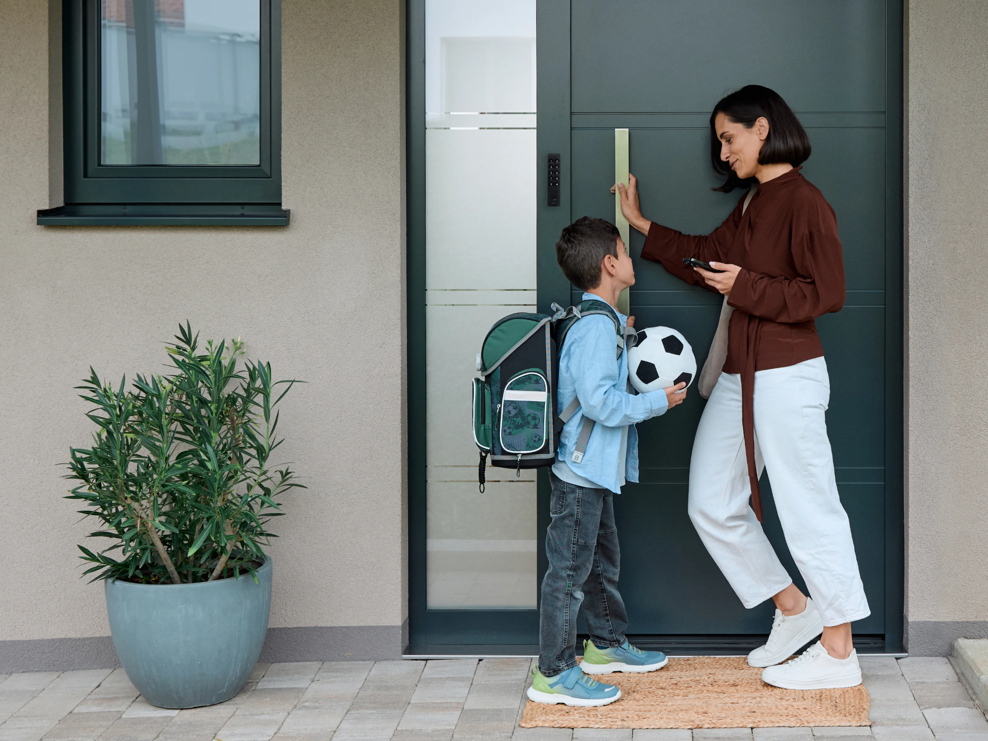 Mother and son at the front door. She uses the Nuki Keypad 2 while he holds a football.