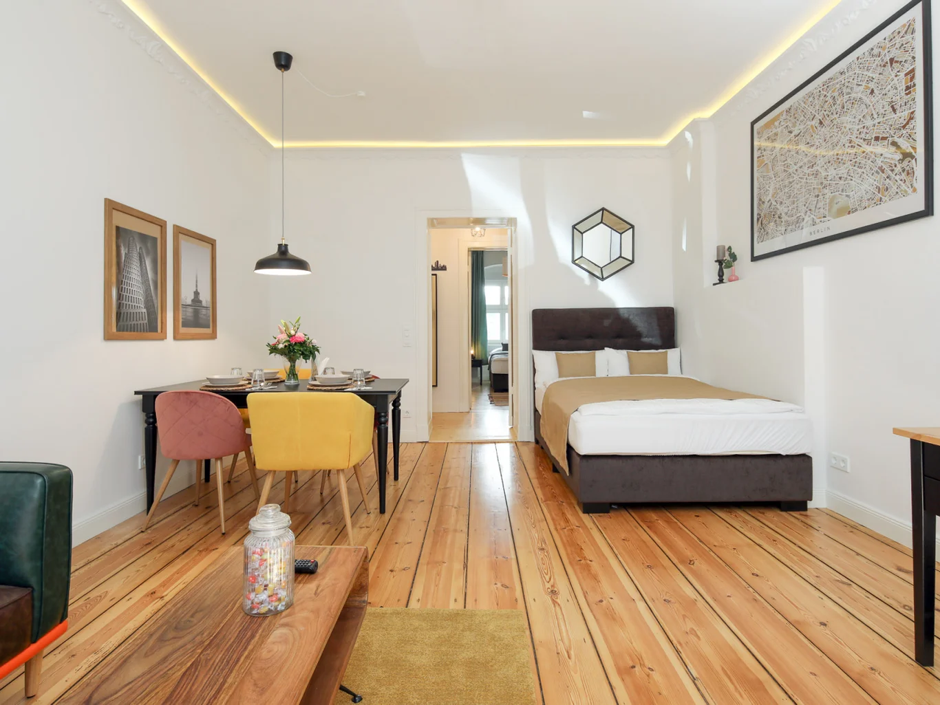 A cozy room with a bed, dining table and a couch. Designed in wood and white.