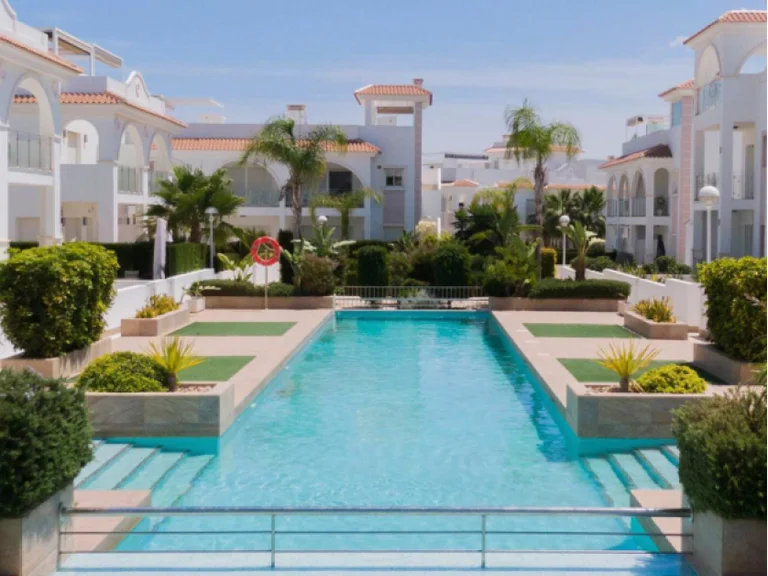 Inside an white stucco appartment complex with a pool and greenery