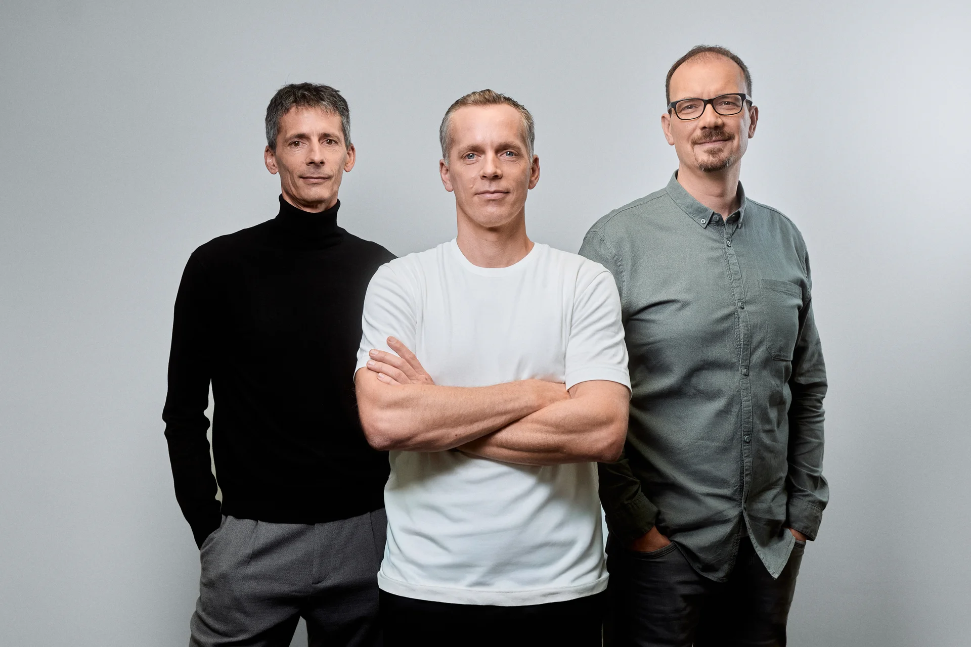 Nuki founders Martin and Jürgen Pansy stand with CTO Claus Diener in front of a light grey background.