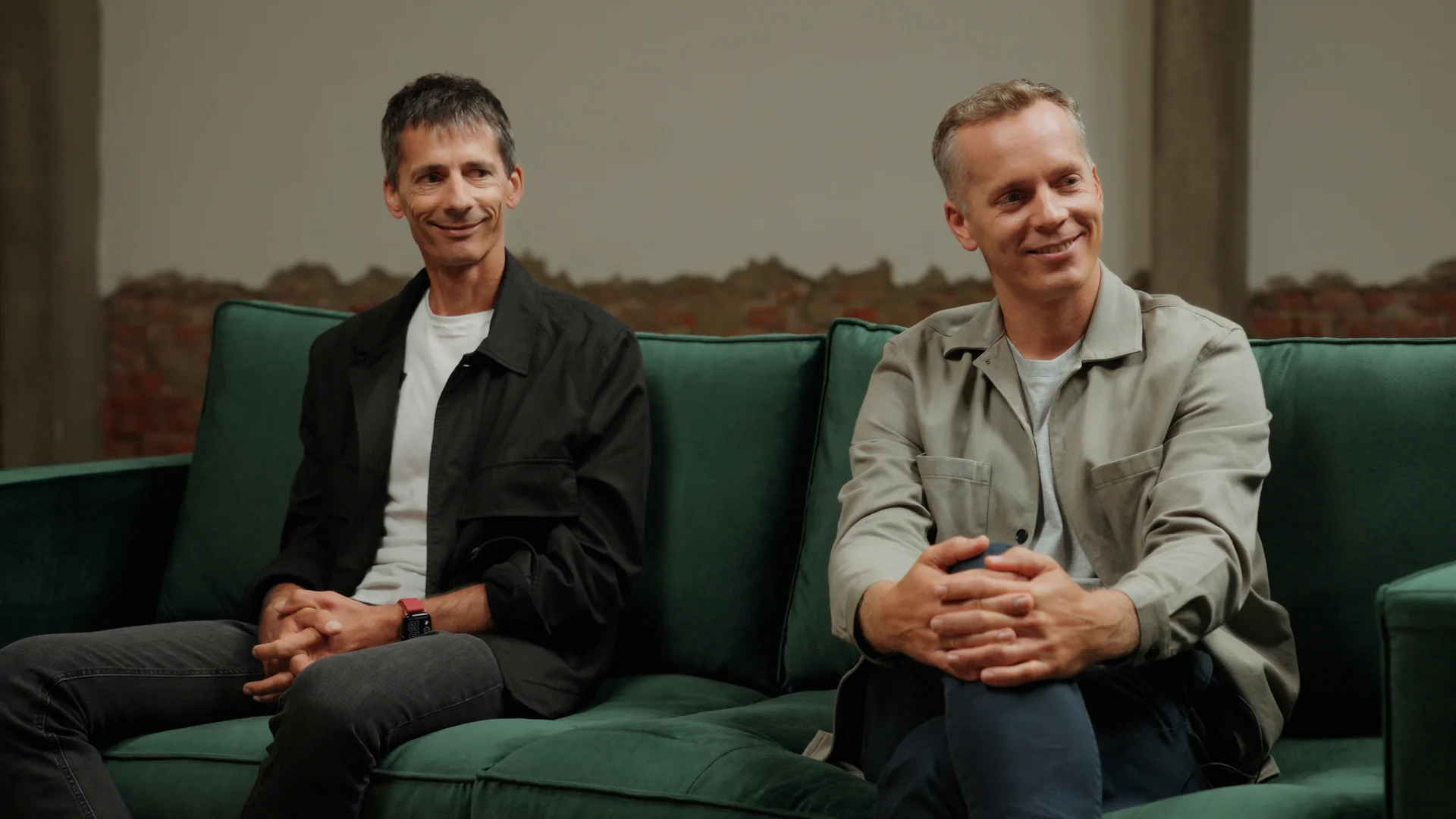 Martin and Jürgen Pansy, founders of Nuki, sit smiling on a green sofa during a relaxed conversation.