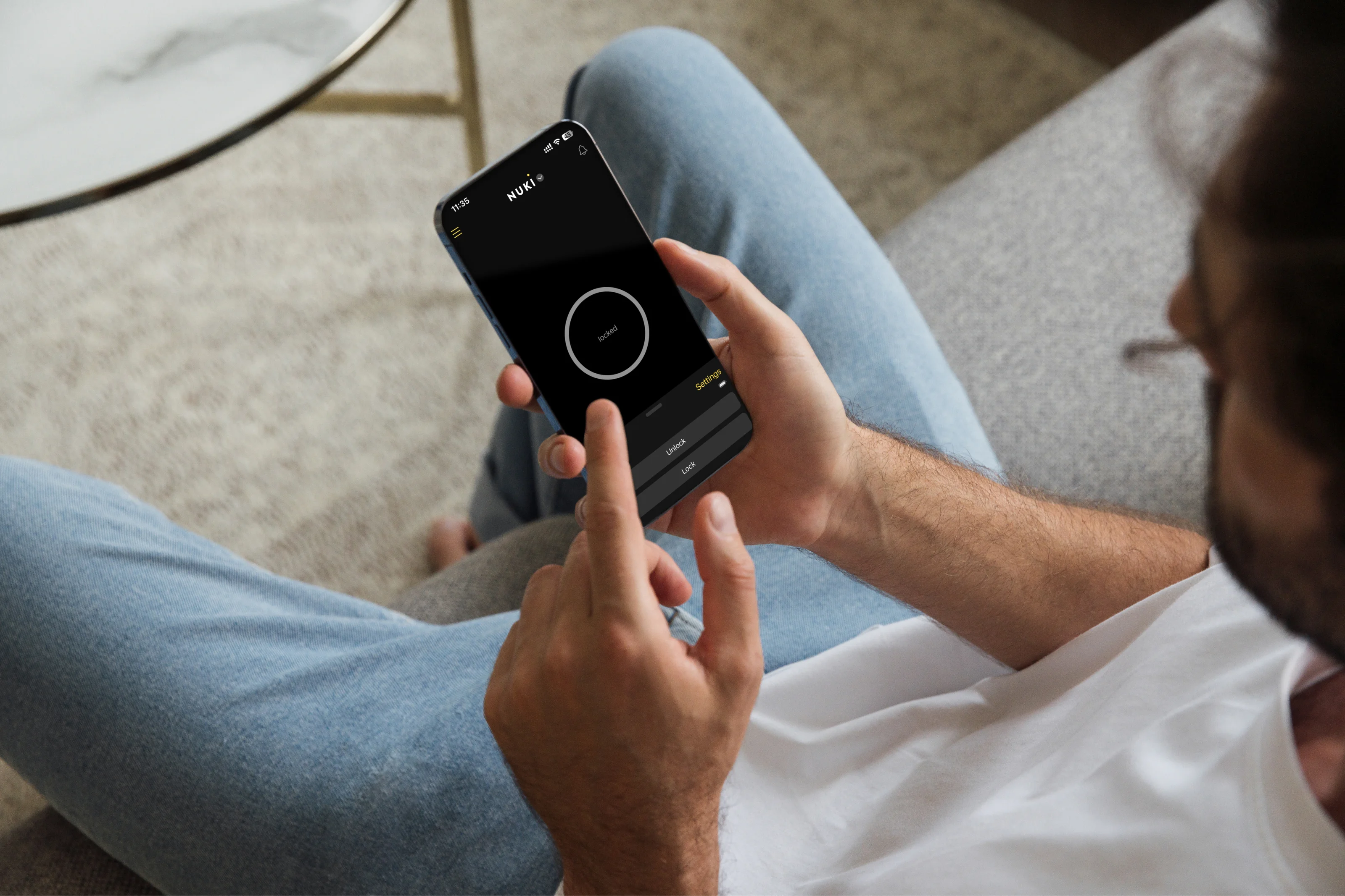 Person steuert das Smart Lock mit der Nuki App per Smartphone vom Sofa aus