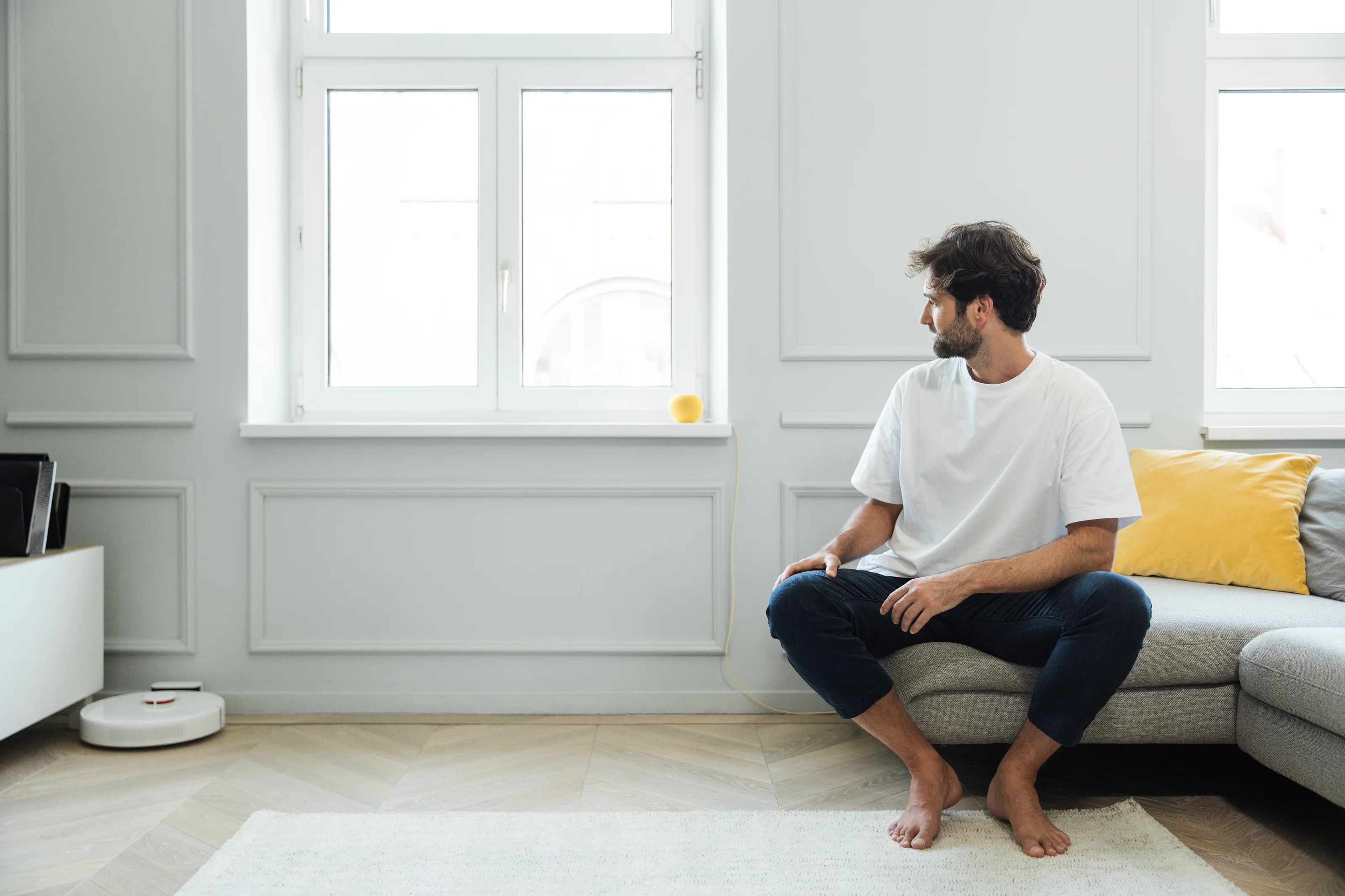 Man sitting on the couch in his smart home looking at a smart speaker.