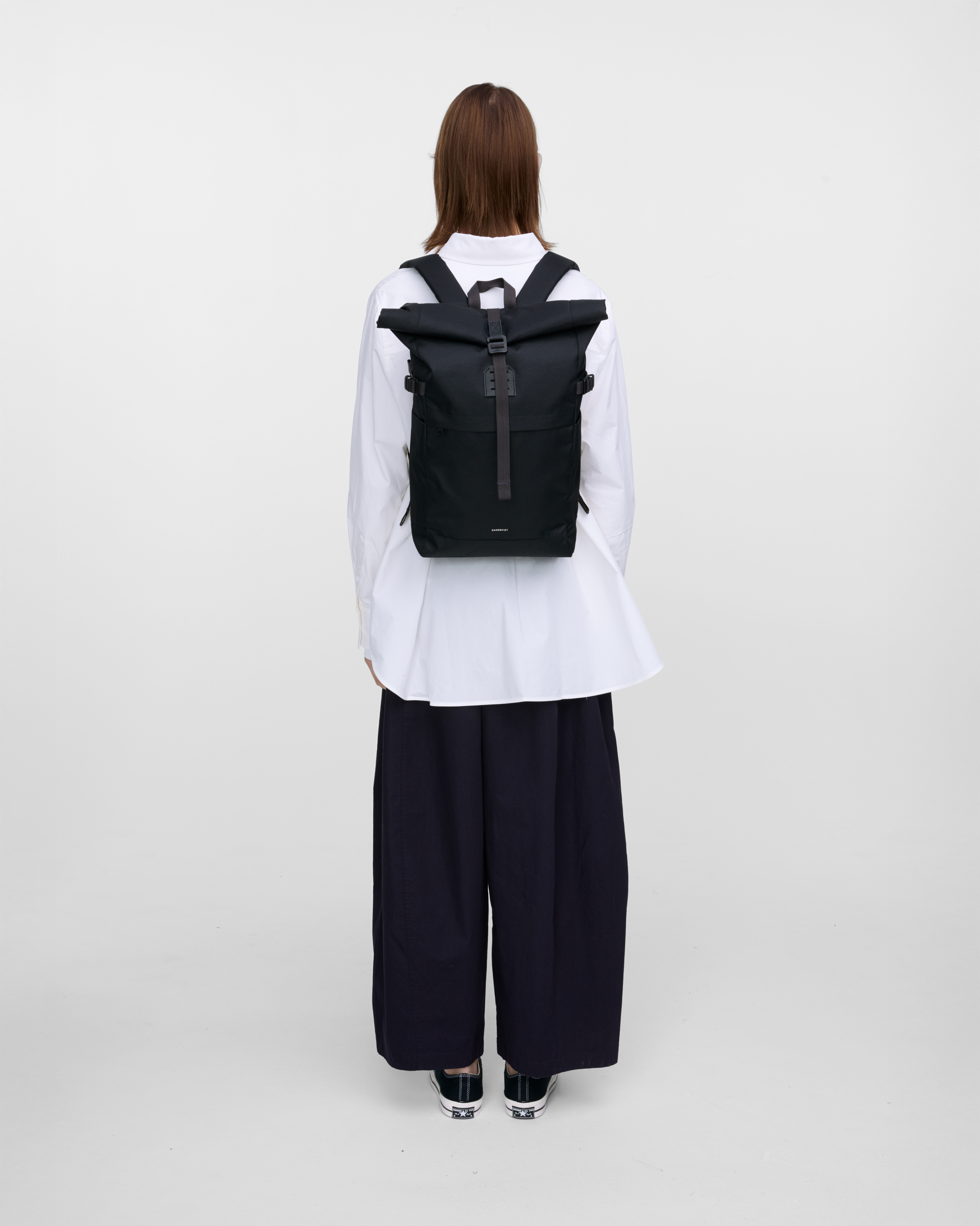 Female model in back view carrying the backpack ICON Rolltop Backpack M in Black showing size and fit. 