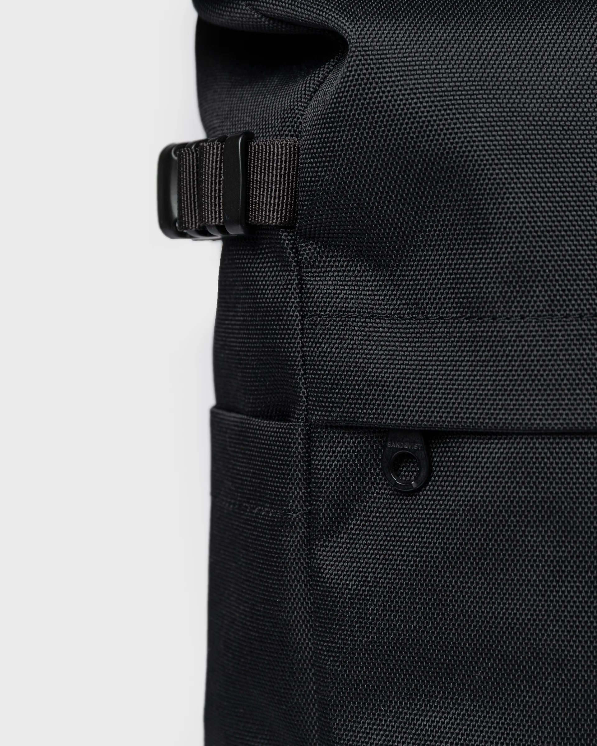 Close up view of adjustable strap, side slip pocket and outer zipper pocket on the backpack Sandqvist ICON Rolltop Backpack M 14" in black.