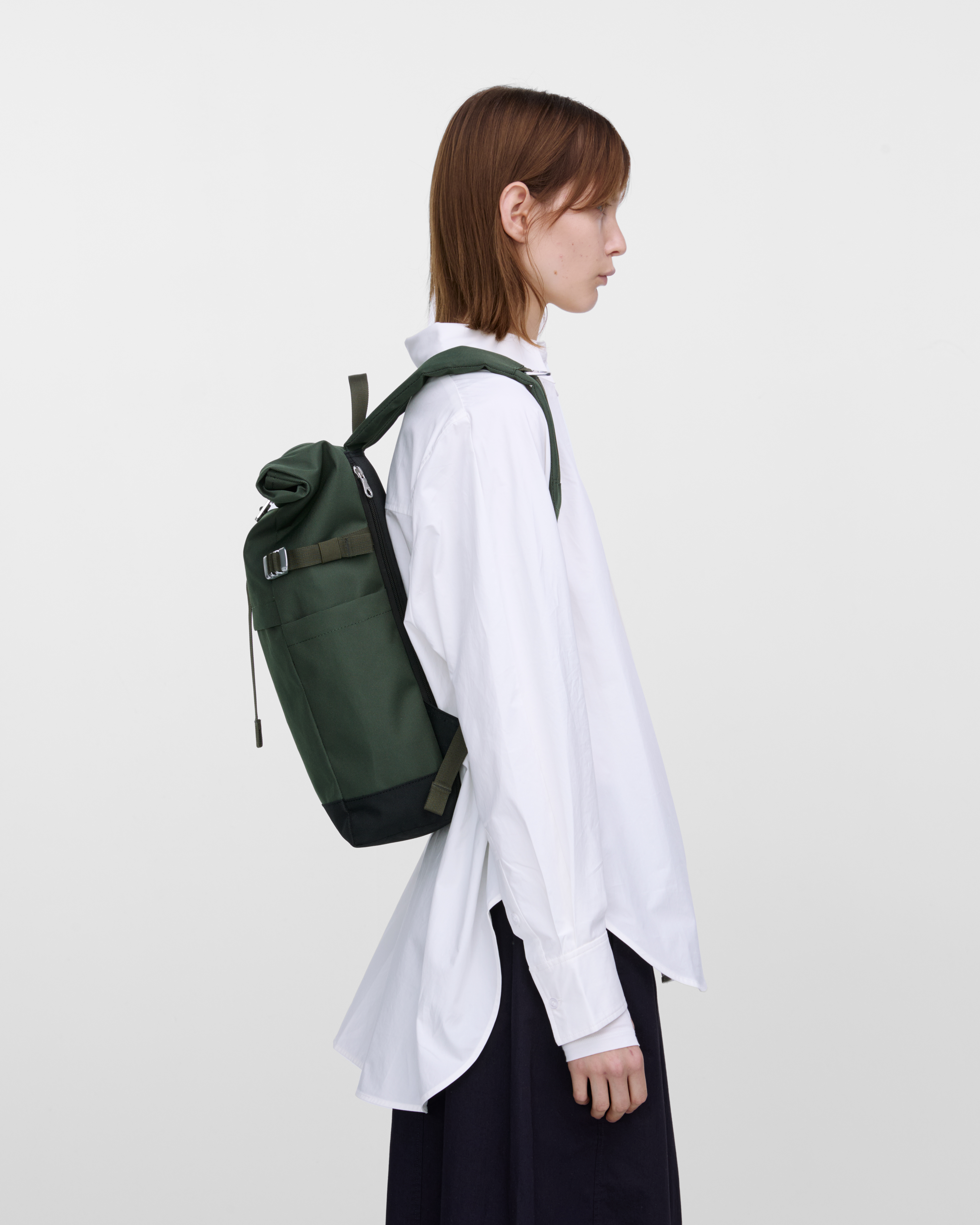 Female model carrying backpack Sandqvist ICON Rolltop Backpack M in dark green, side view showing fit and size. 