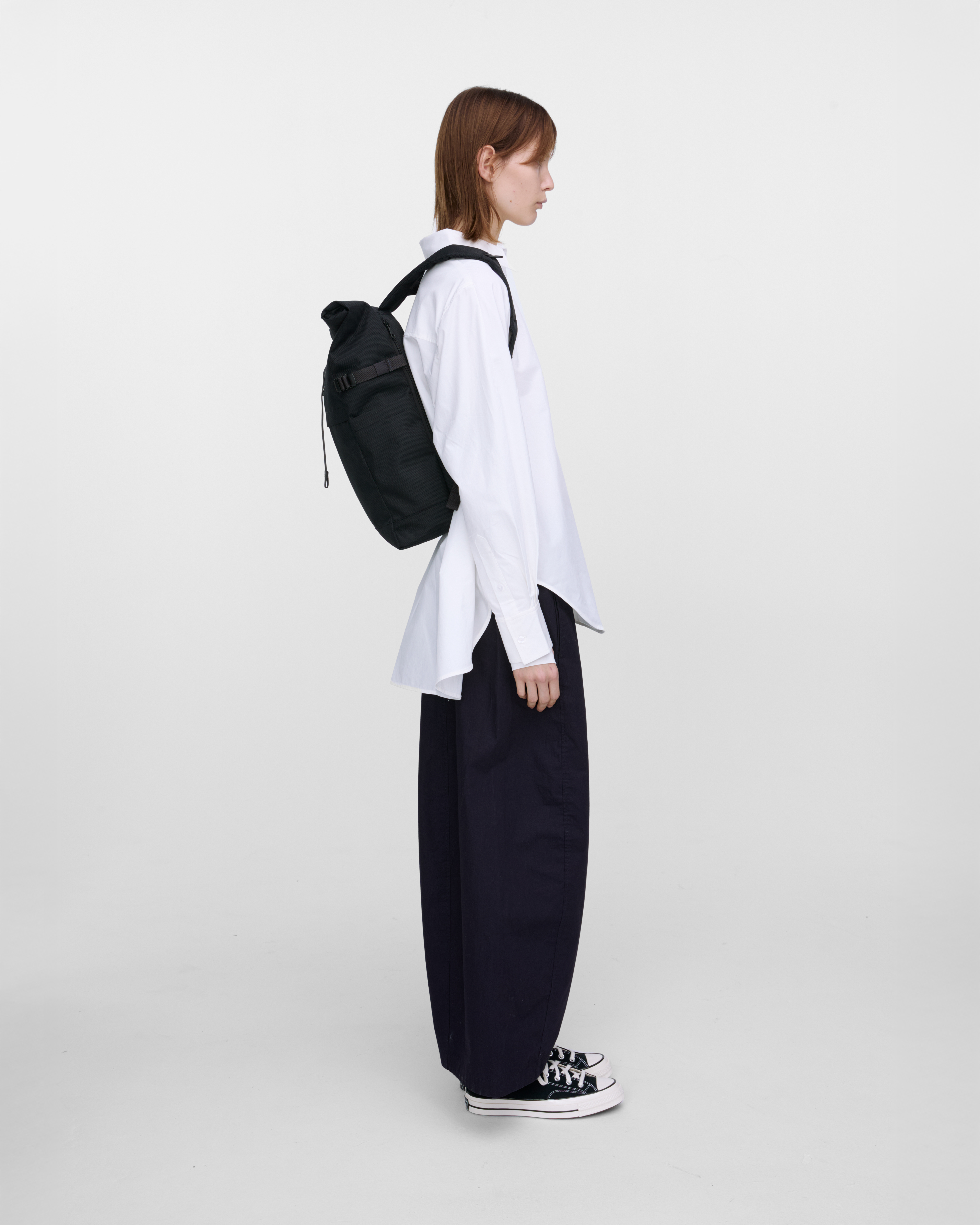 Female model carrying backpack Sandqvist ICON Rolltop Backpack M in black, side view showing fit and size. 