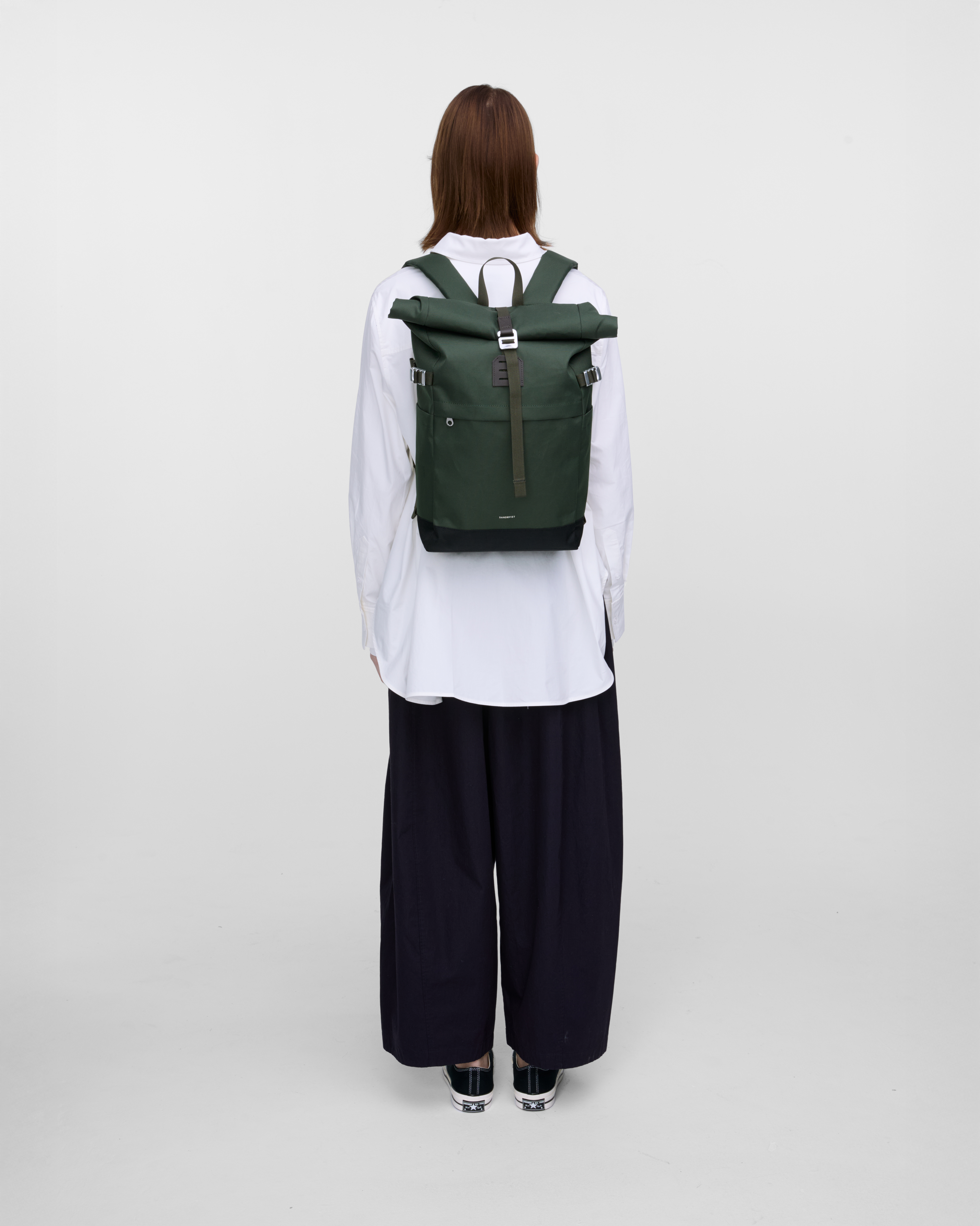Female model in back view carrying the backpack ICON Rolltop Backpack M in Dark Green showing size and fit. 