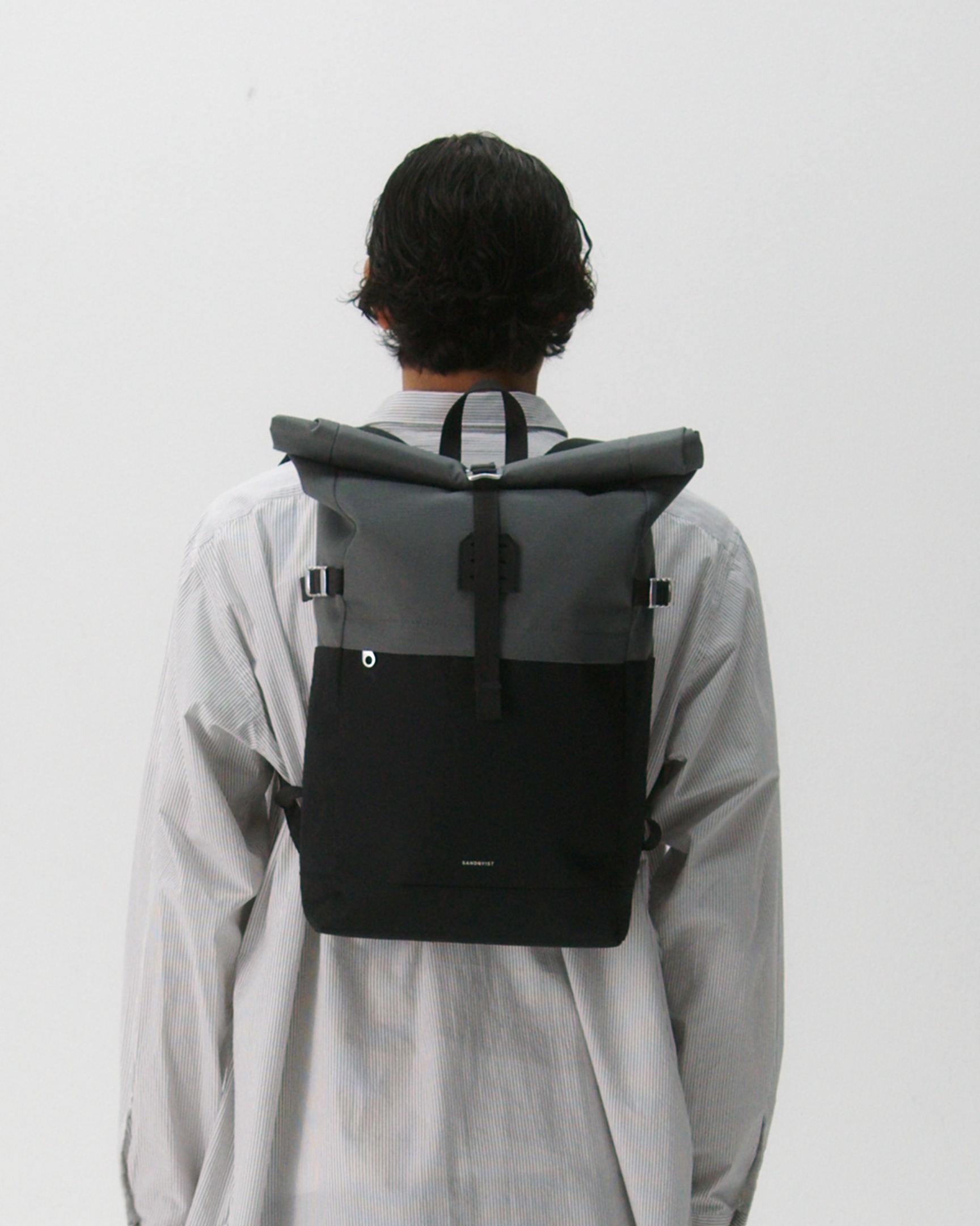 Male model carrying the backpack ICON Rolltop Backpack M, Grey and black. Back view showing fit and size. 