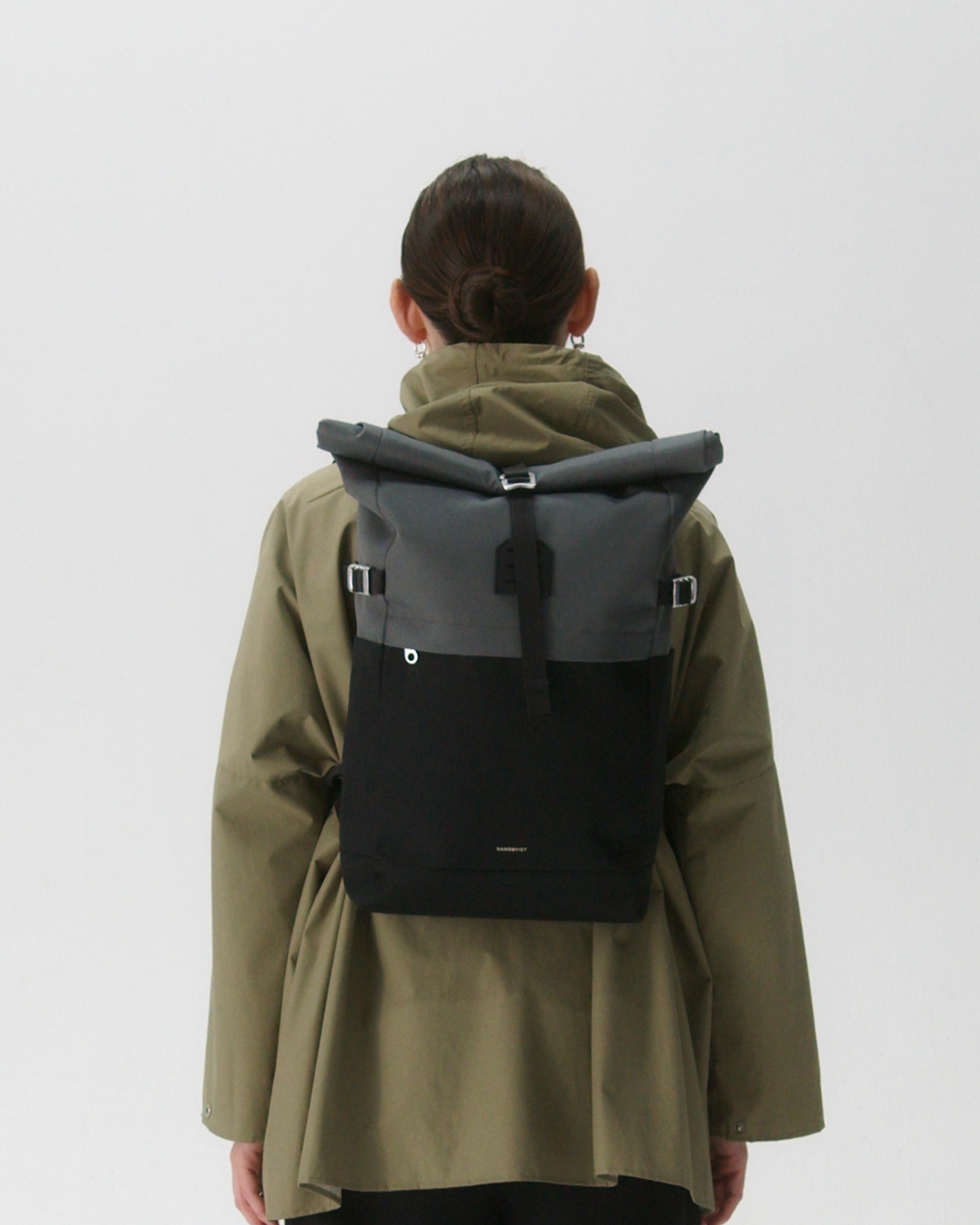 Female model in back view carrying the backpack ICON Rolltop Backpack M in Grey and black showing size and fit. 