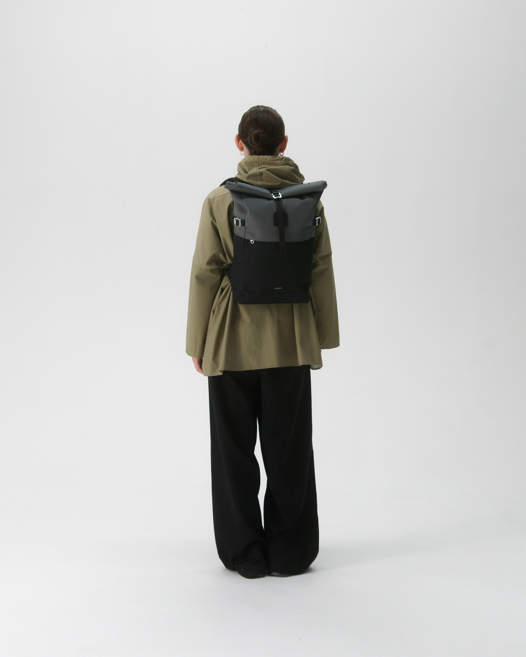 Female model in back view carrying the backpack ICON Rolltop Backpack M in Grey and black showing size and fit. 