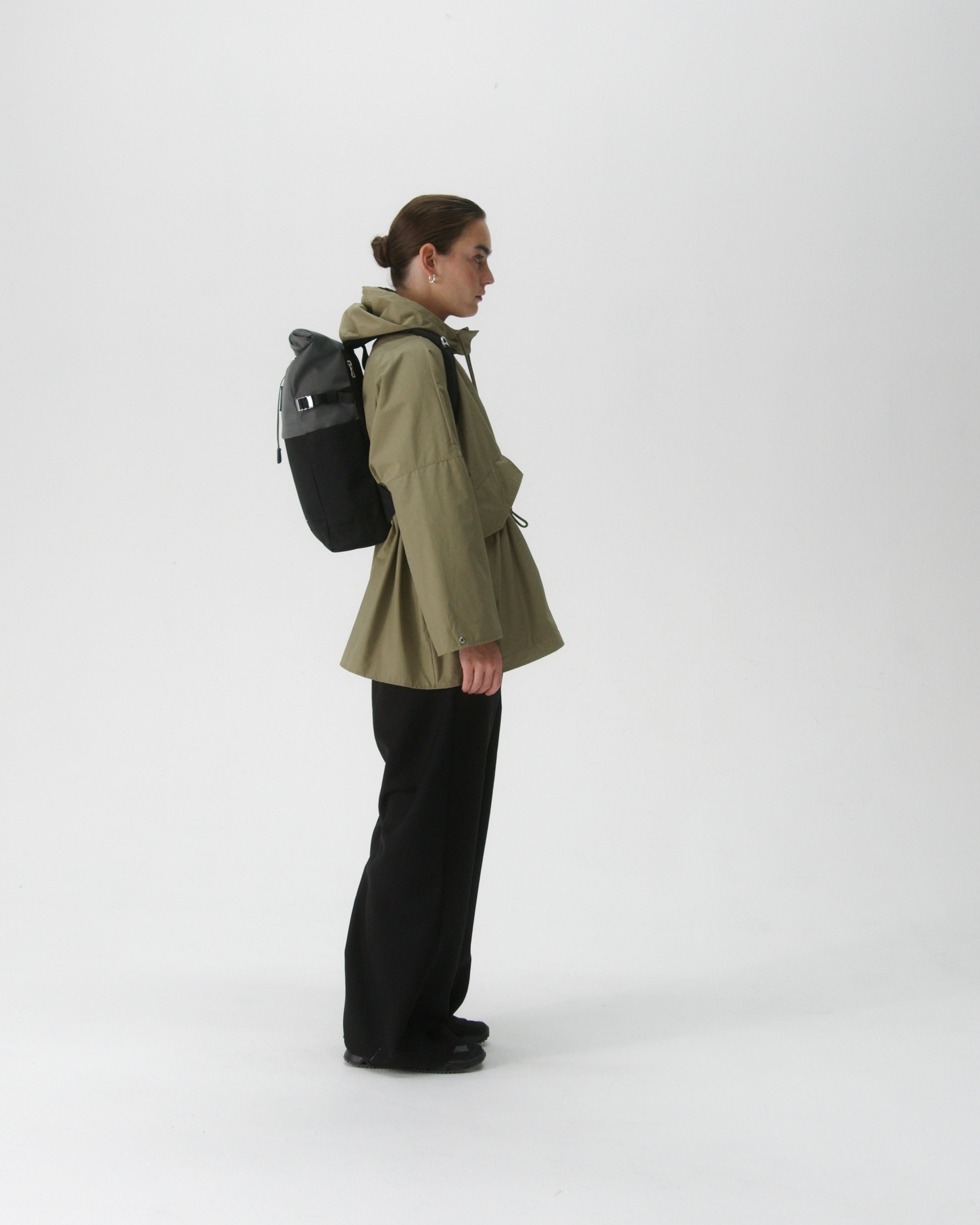 Female model carrying backpack Sandqvist ICON Rolltop Backpack M in grey and black, side view showing fit and size. 