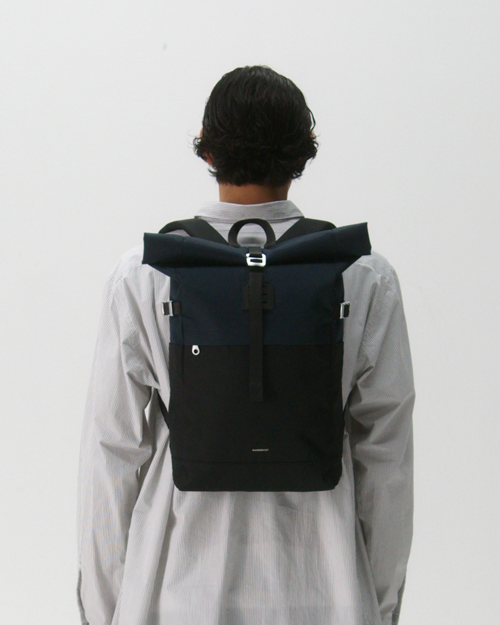 Male model carrying the backpack ICON Rolltop Backpack M, Dark blue and black. Back view showing fit and size. 