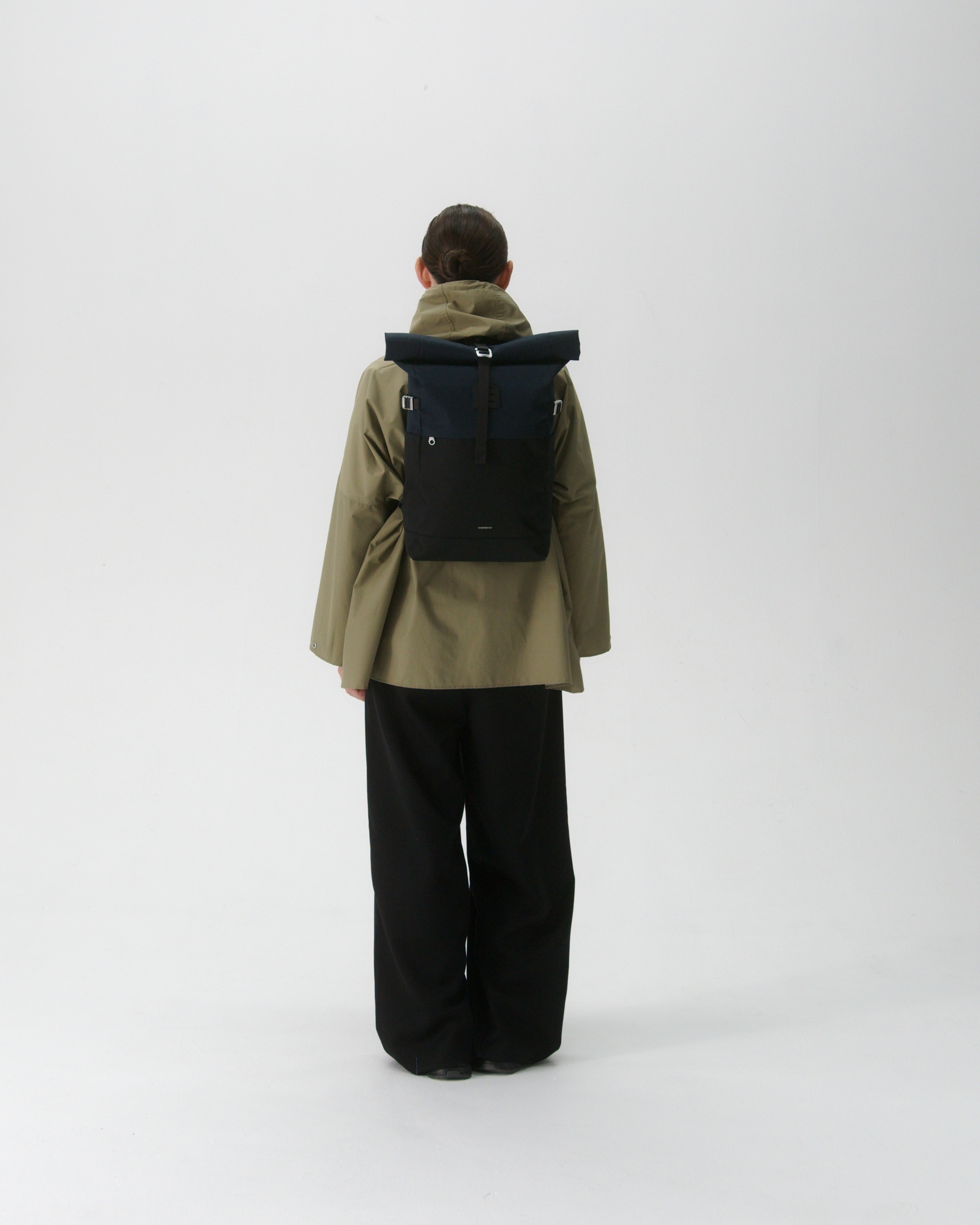 Female model in back view carrying the backpack ICON Rolltop Backpack M in Blue and black showing size and fit. 