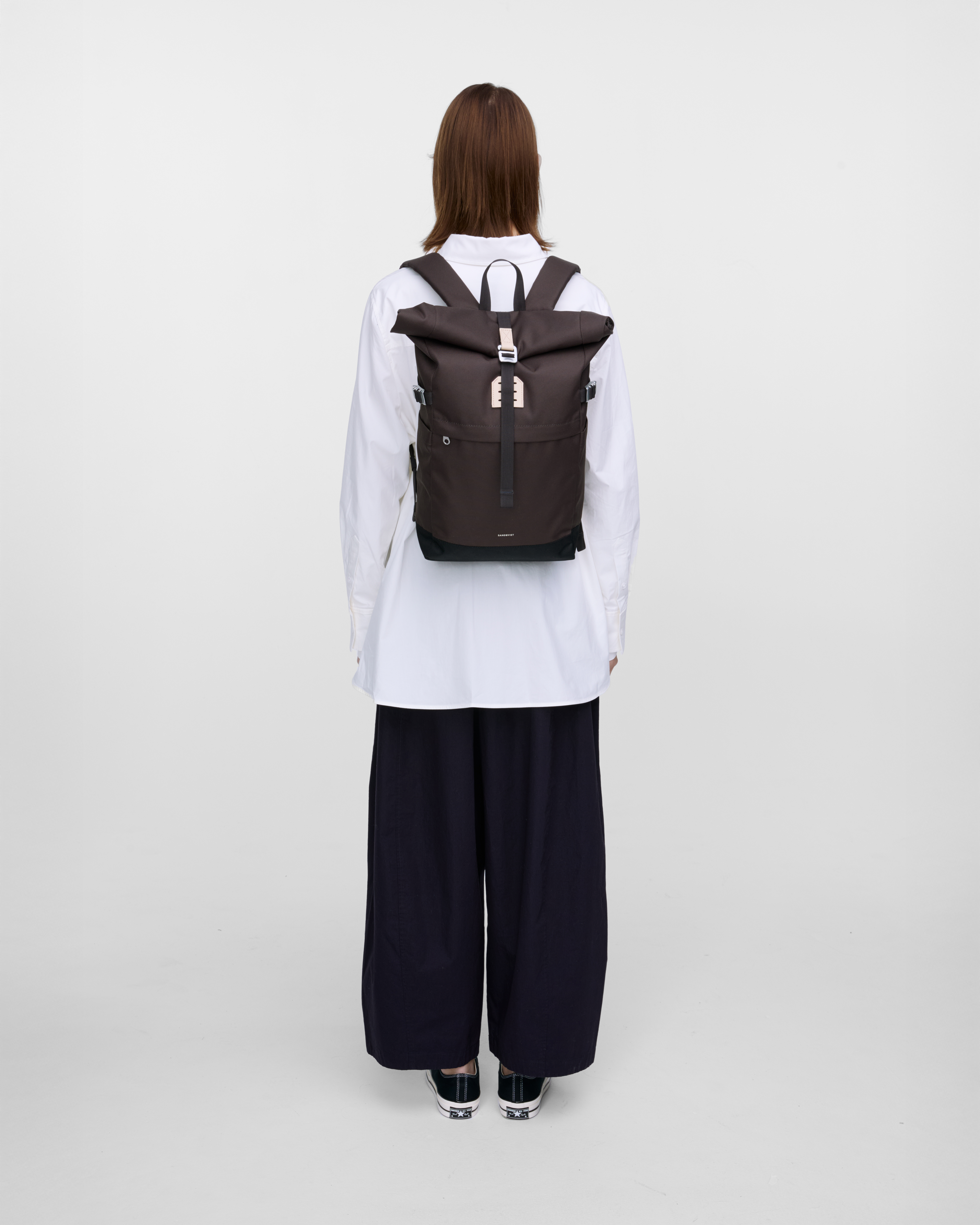 Female model in back view carrying the backpack ICON Rolltop Backpack M in Brown showing size and fit. 